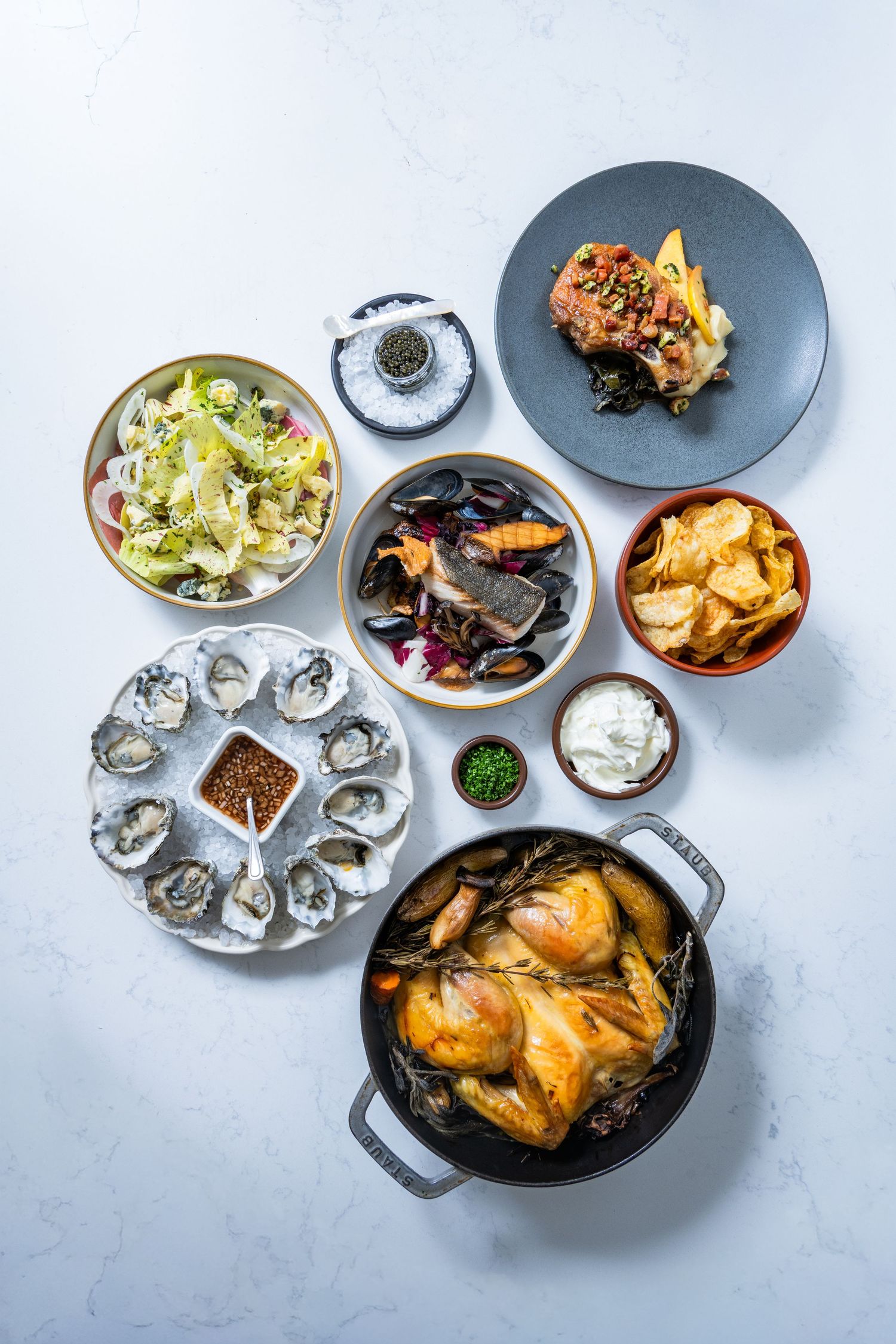 Overhead food spread with oysters, roast chicken, and sides, photographed for restaurant menu and editorial use.