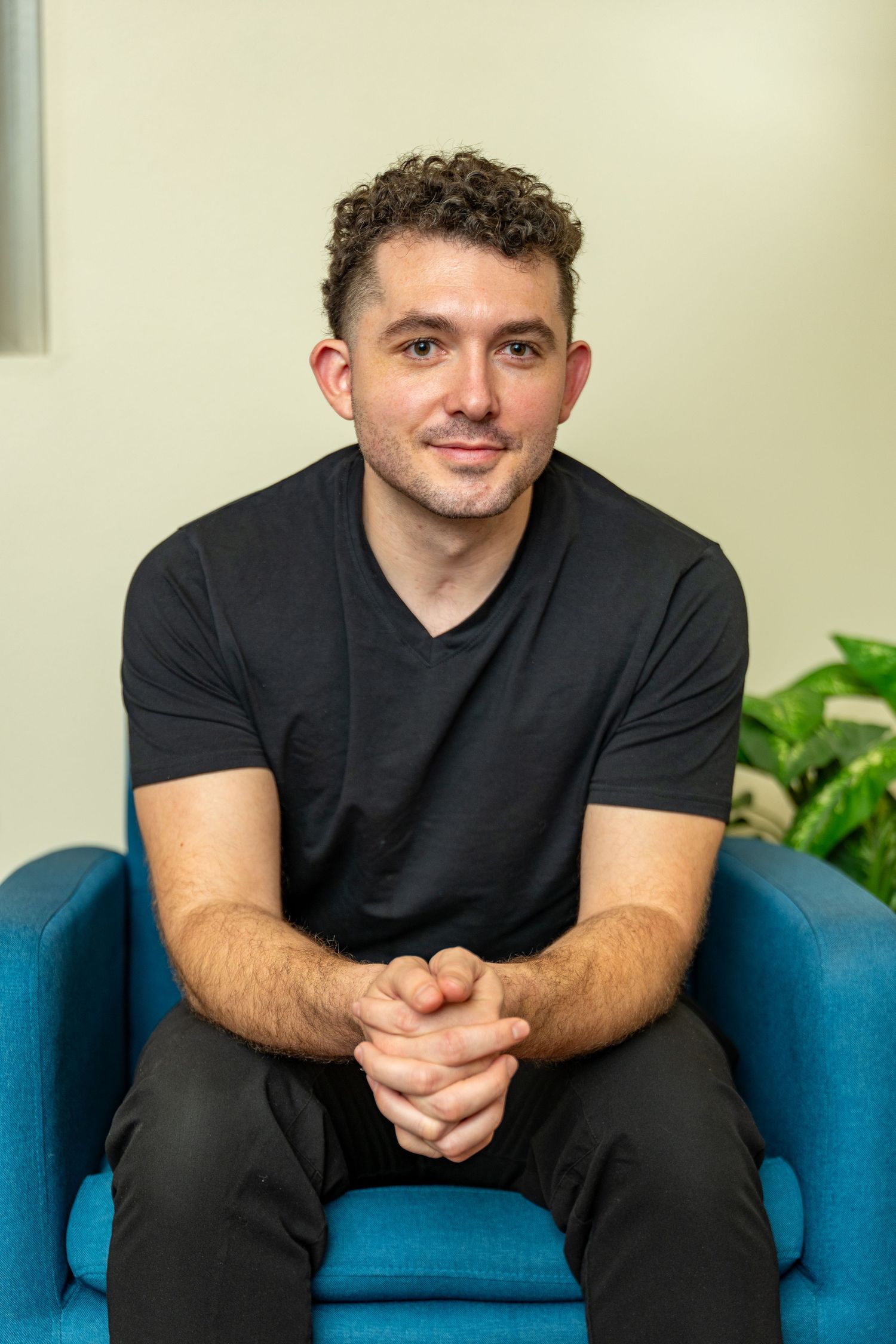 Professional headshot of man seated in modern office chair, natural light portrait with clean background for corporate branding.