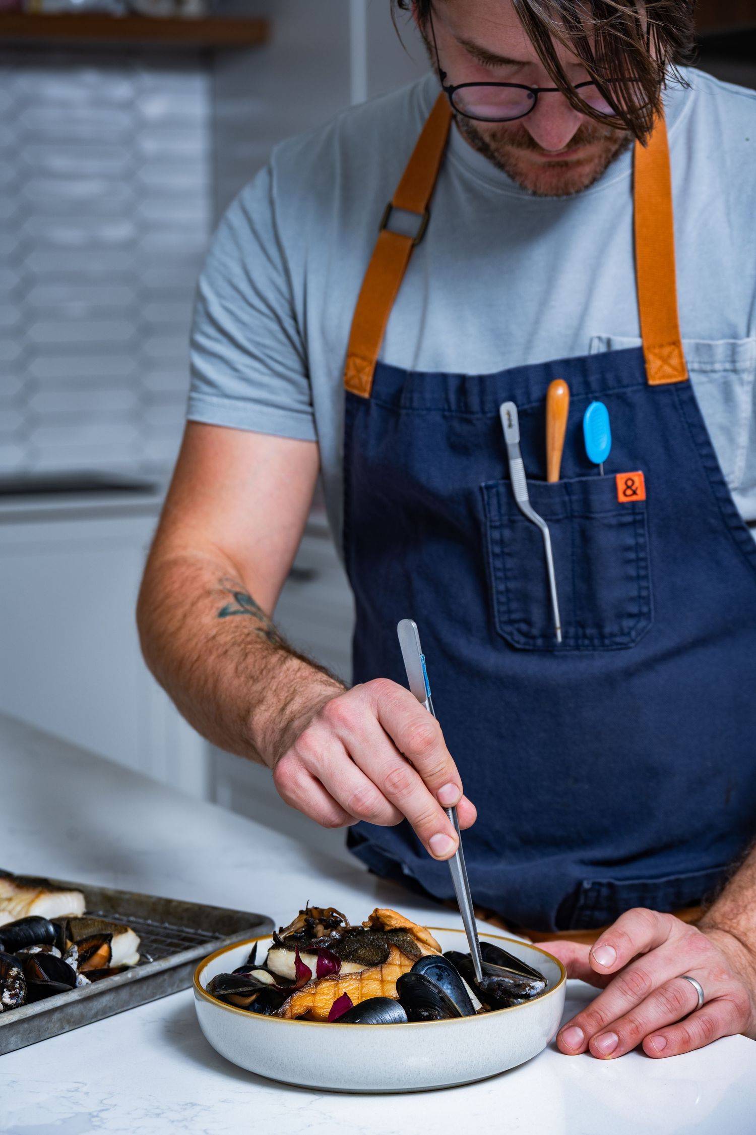 Chef plating seafood dish with tweezers, photographed for fine dining branding and editorial food content.