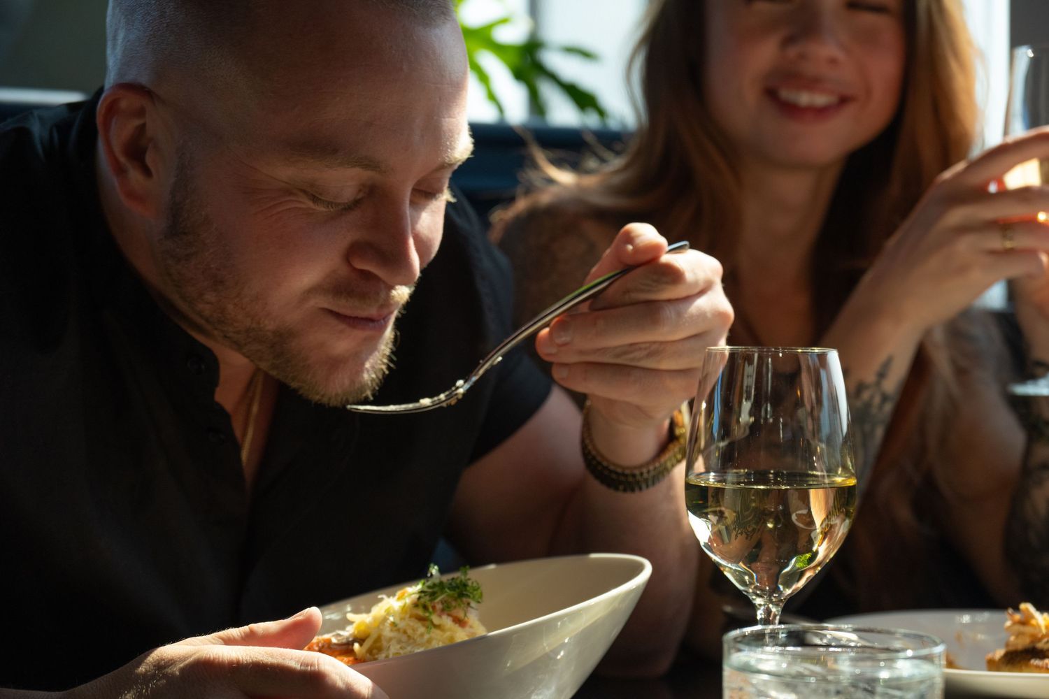 Lifestyle restaurant scene of couple dining with wine and pasta in warm natural window light.