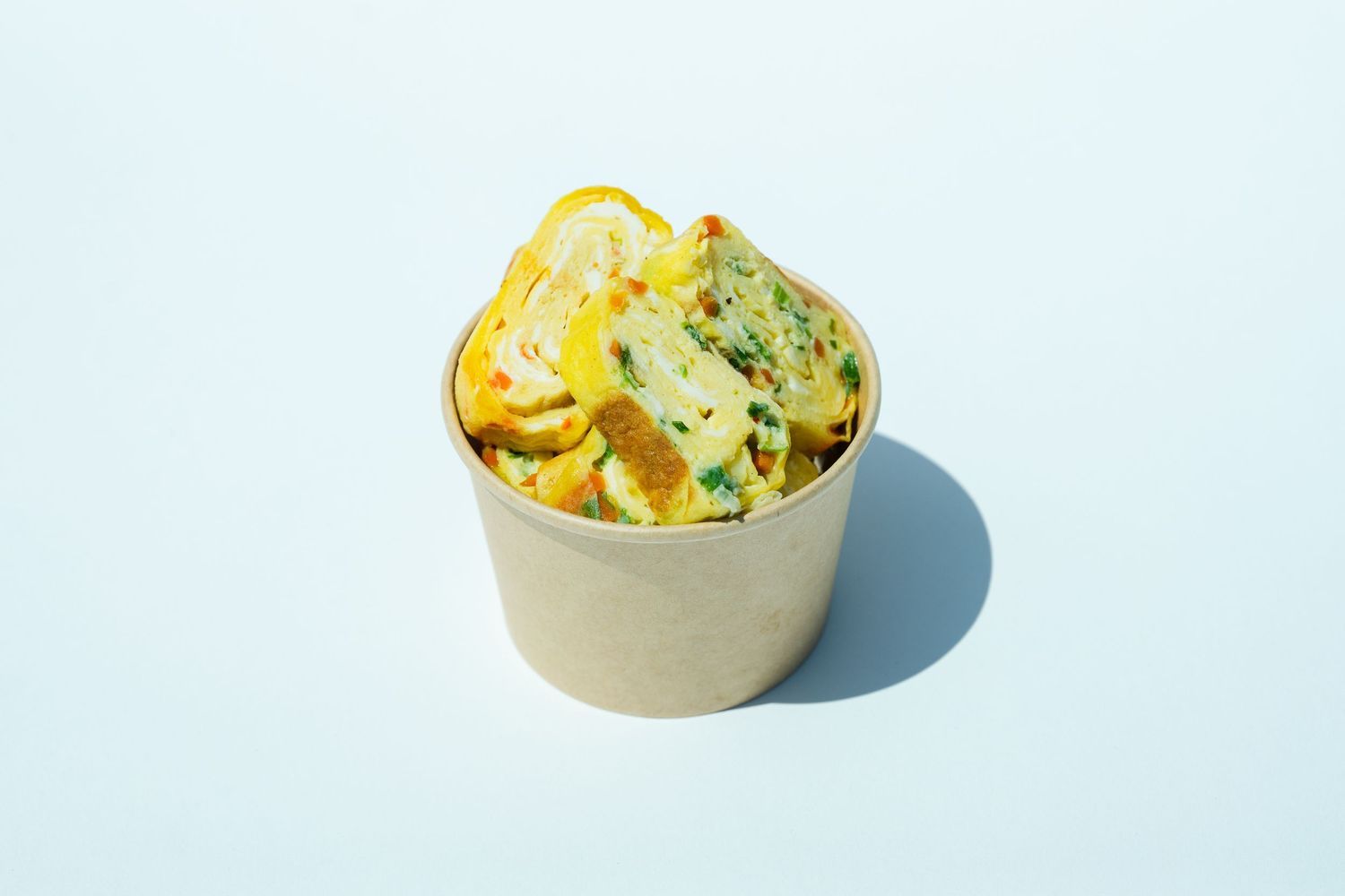 Korean rolled omelet in compostable takeout cup, styled for restaurant menu photography and brand marketing.