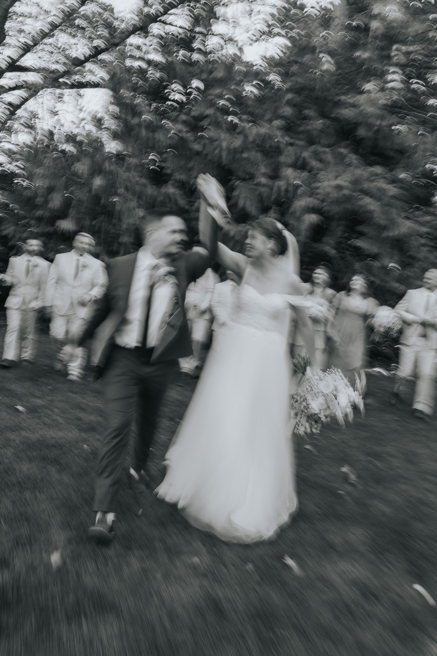 Black and white motion photo of the couple celebrating as the bridal party walks behind them