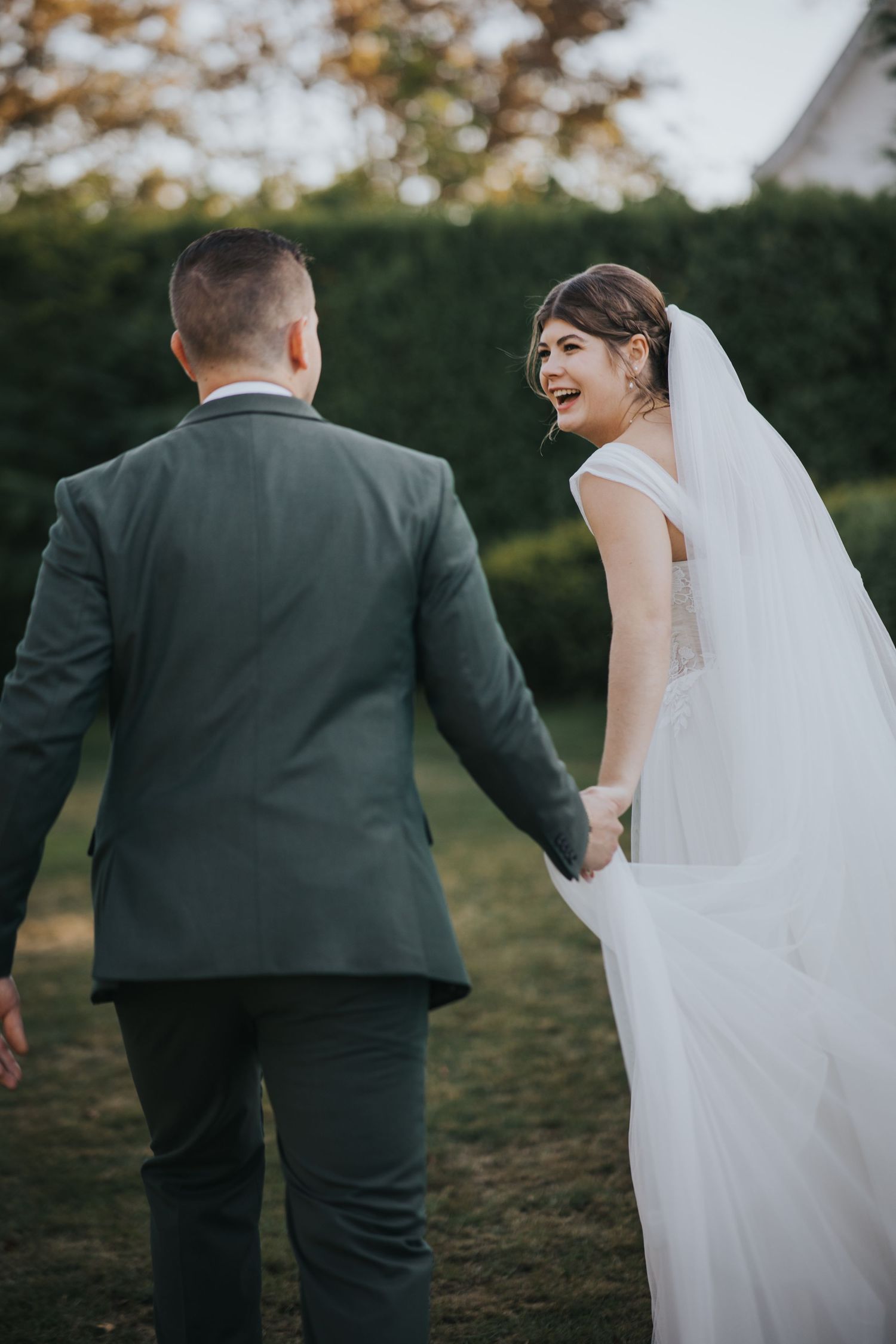 Bride laughing over her shoulder as she walks hand in hand with the groom