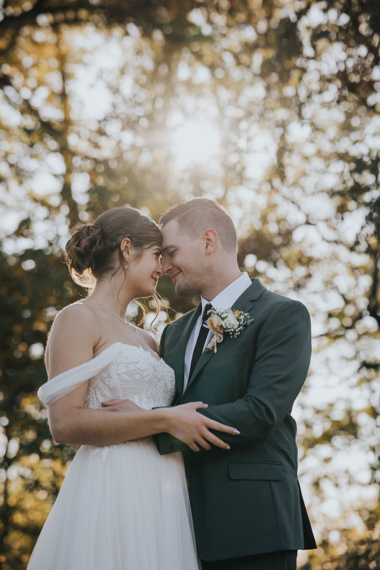 Bride and groom touching foreheads with sunlight glowing through the trees behind them
