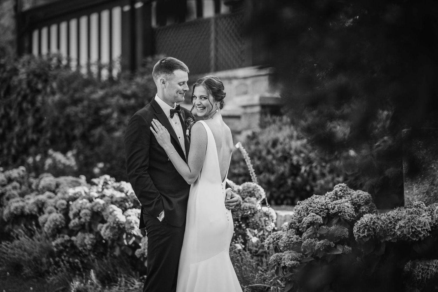 Black and white photo of a bride and groom embracing in a garden surrounded by blooming hydrangeas.