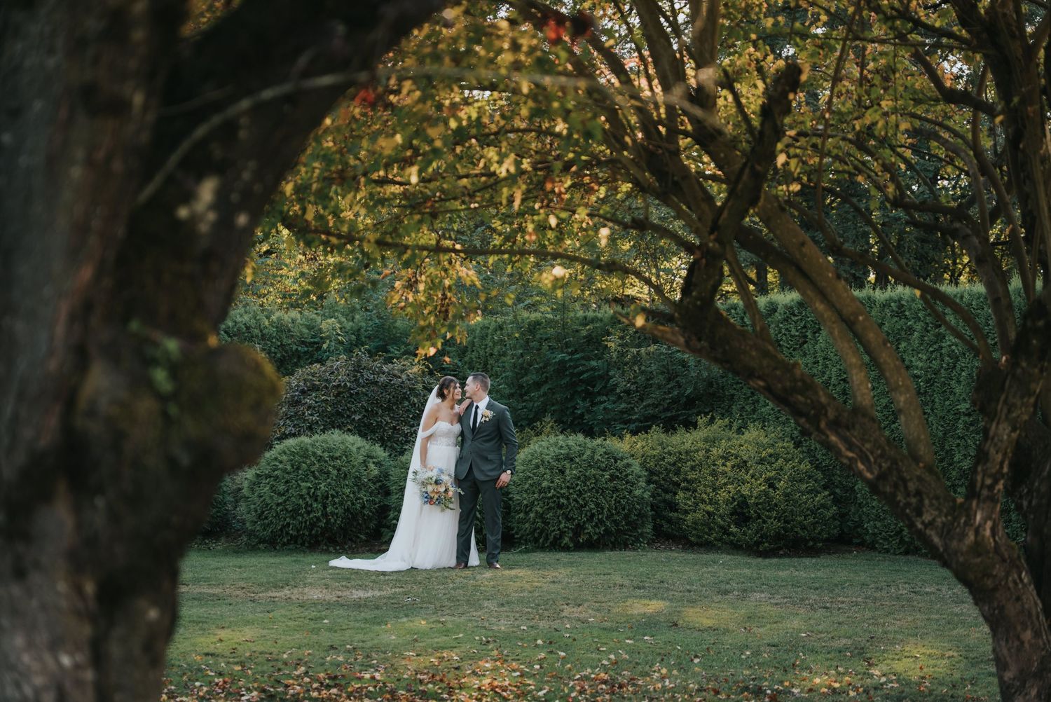 Bride and groom framed by tree branches in the gardens of Estate 248