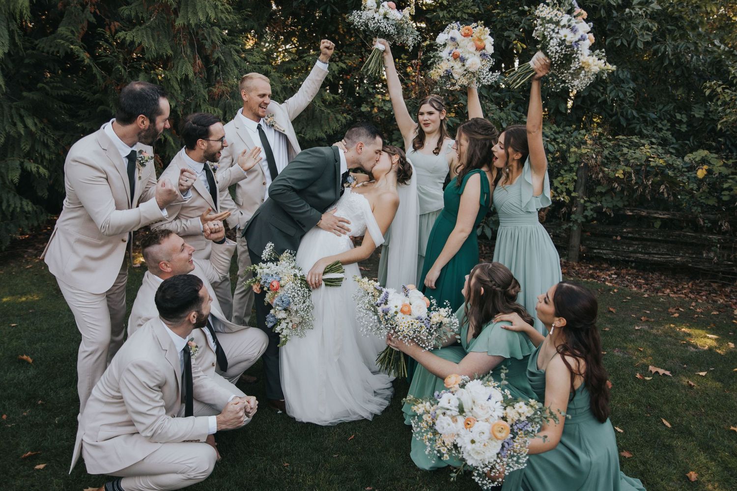 Bridal party cheering with bouquets raised as the groom dips the bride for a kiss