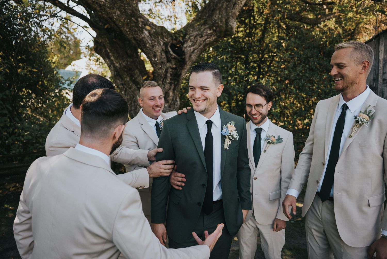 Groom laughing as his groomsmen gather around him before the ceremony