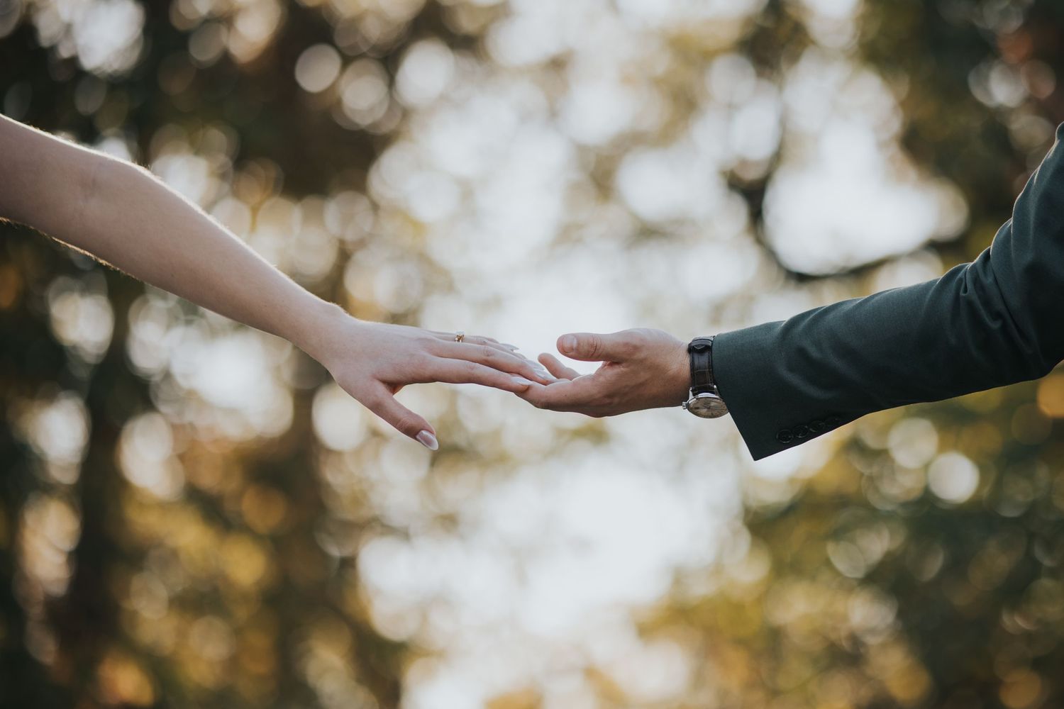 Bride and groom's hands reaching for each other against a soft golden background