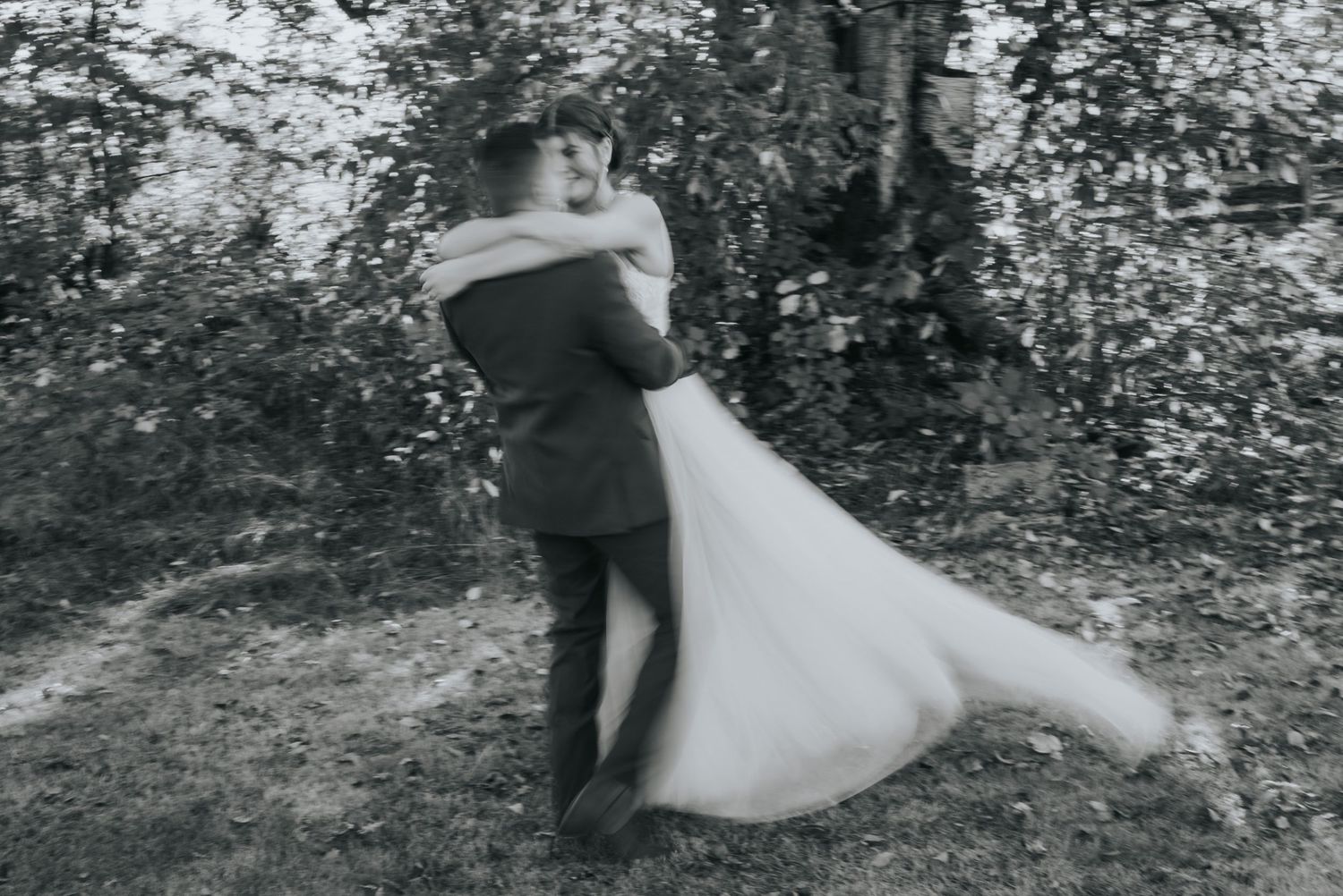 Black and white motion-blur photo of the groom spinning the bride with her dress flowing