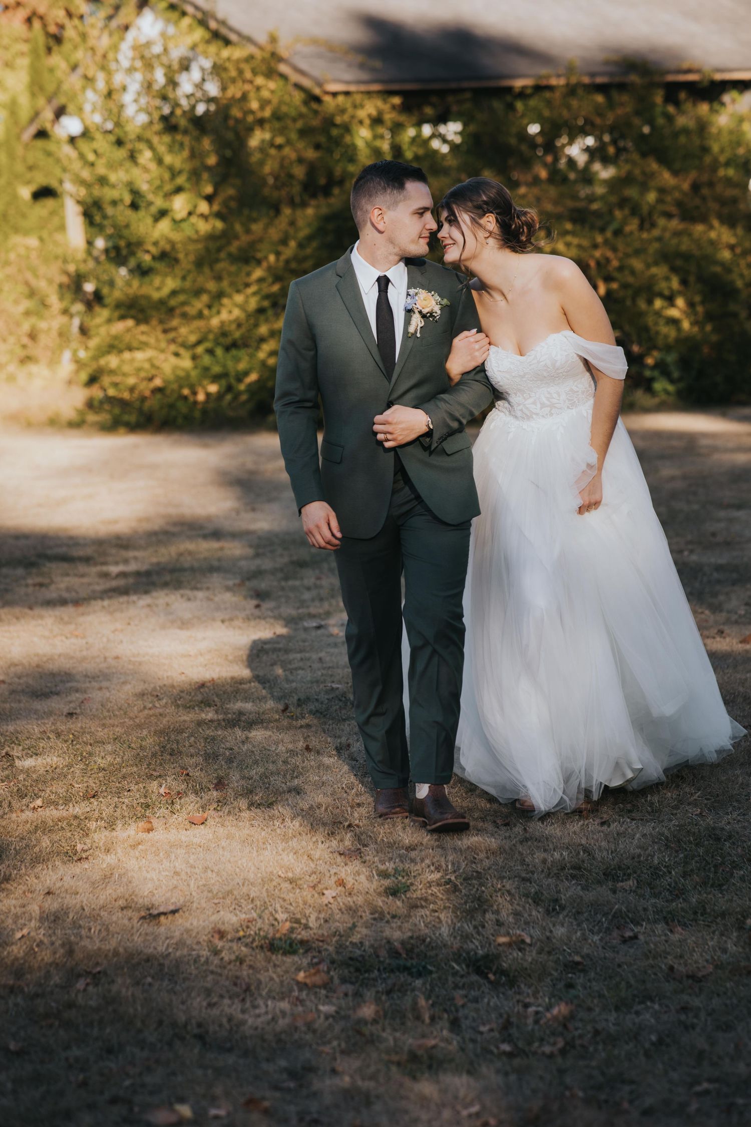 Bride and groom walking arm in arm and smiling at each other in late-afternoon sun