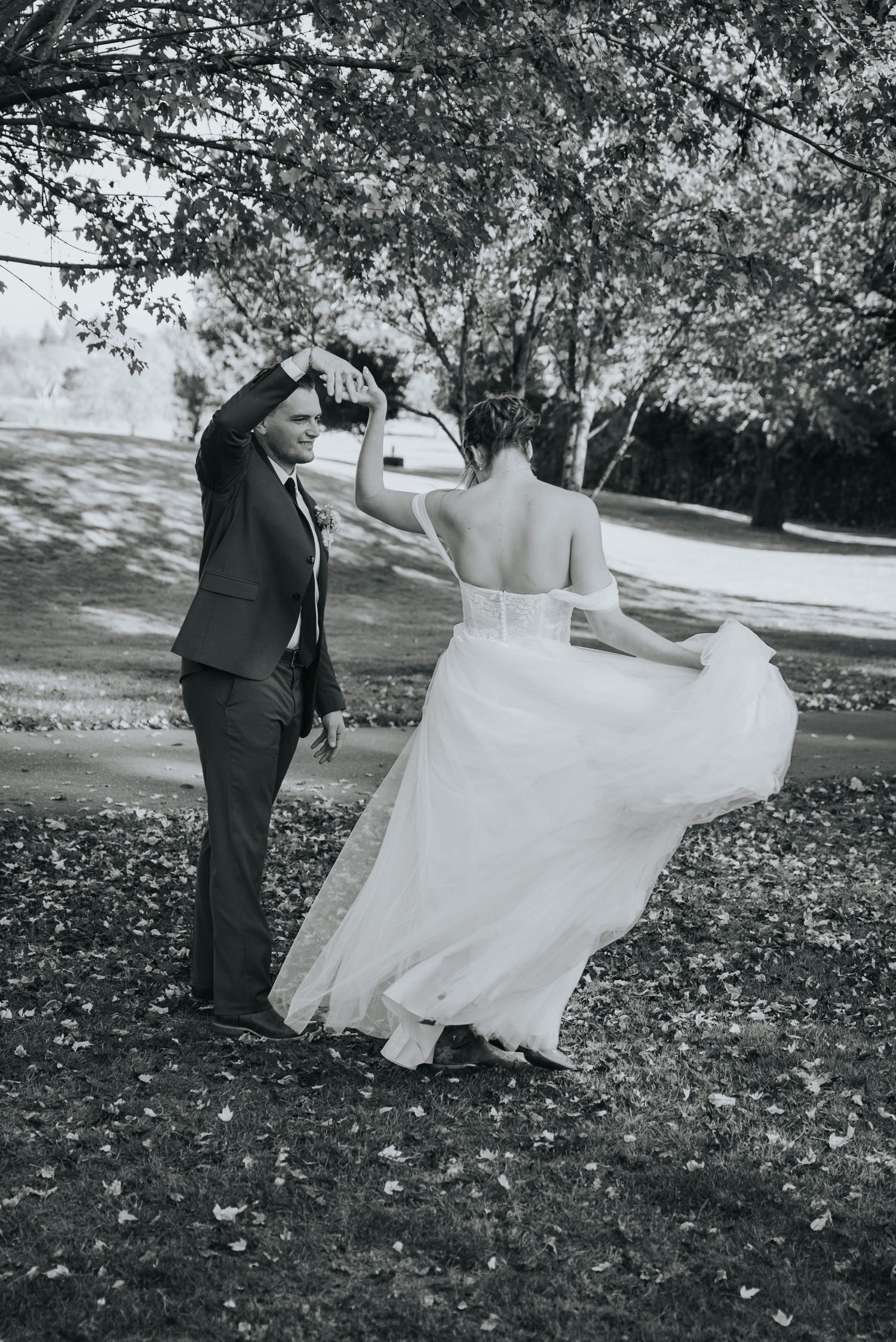 Black and white photo of the groom twirling the bride under the trees