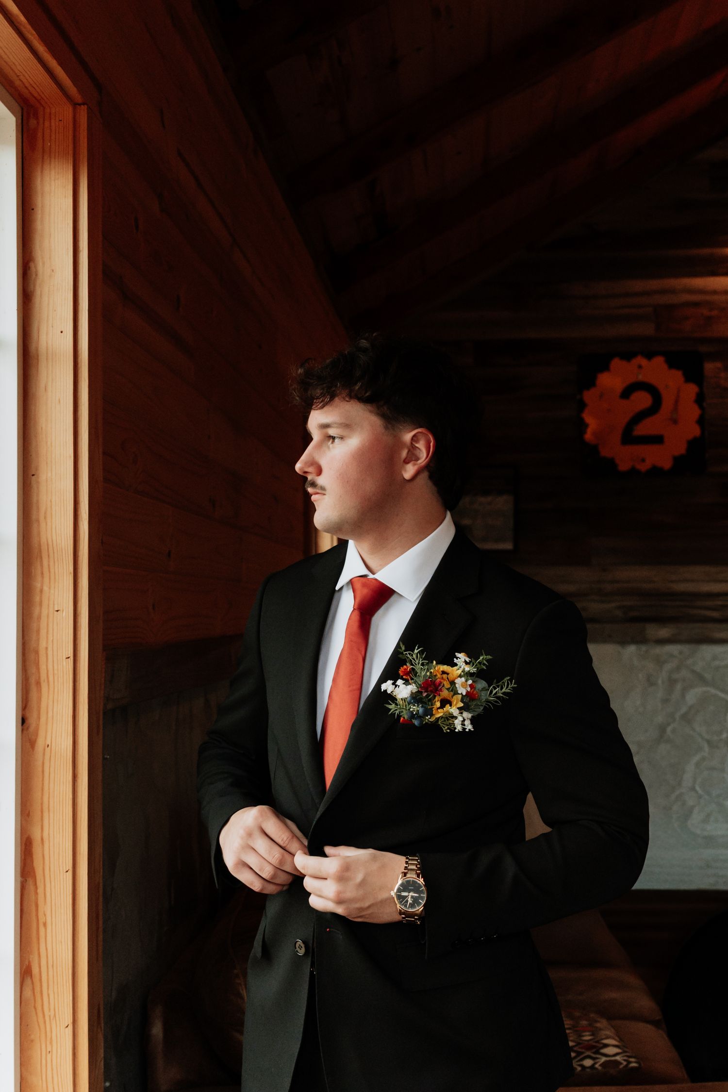 Wedding preparation detail shot of formal attire with orange tie and boutonniere.