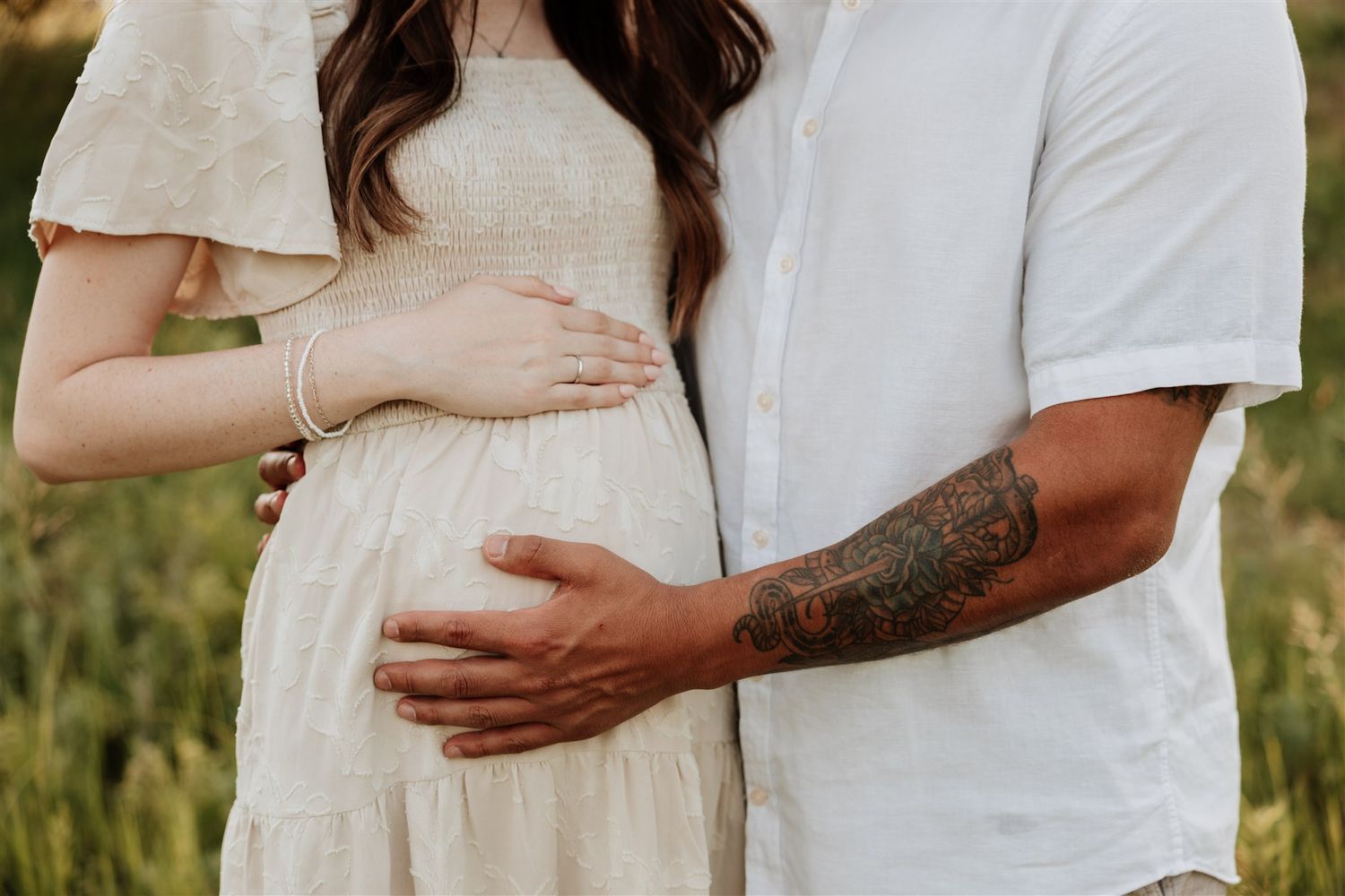 Intimate maternity photos showing couple embracing in white clothing outdoors.