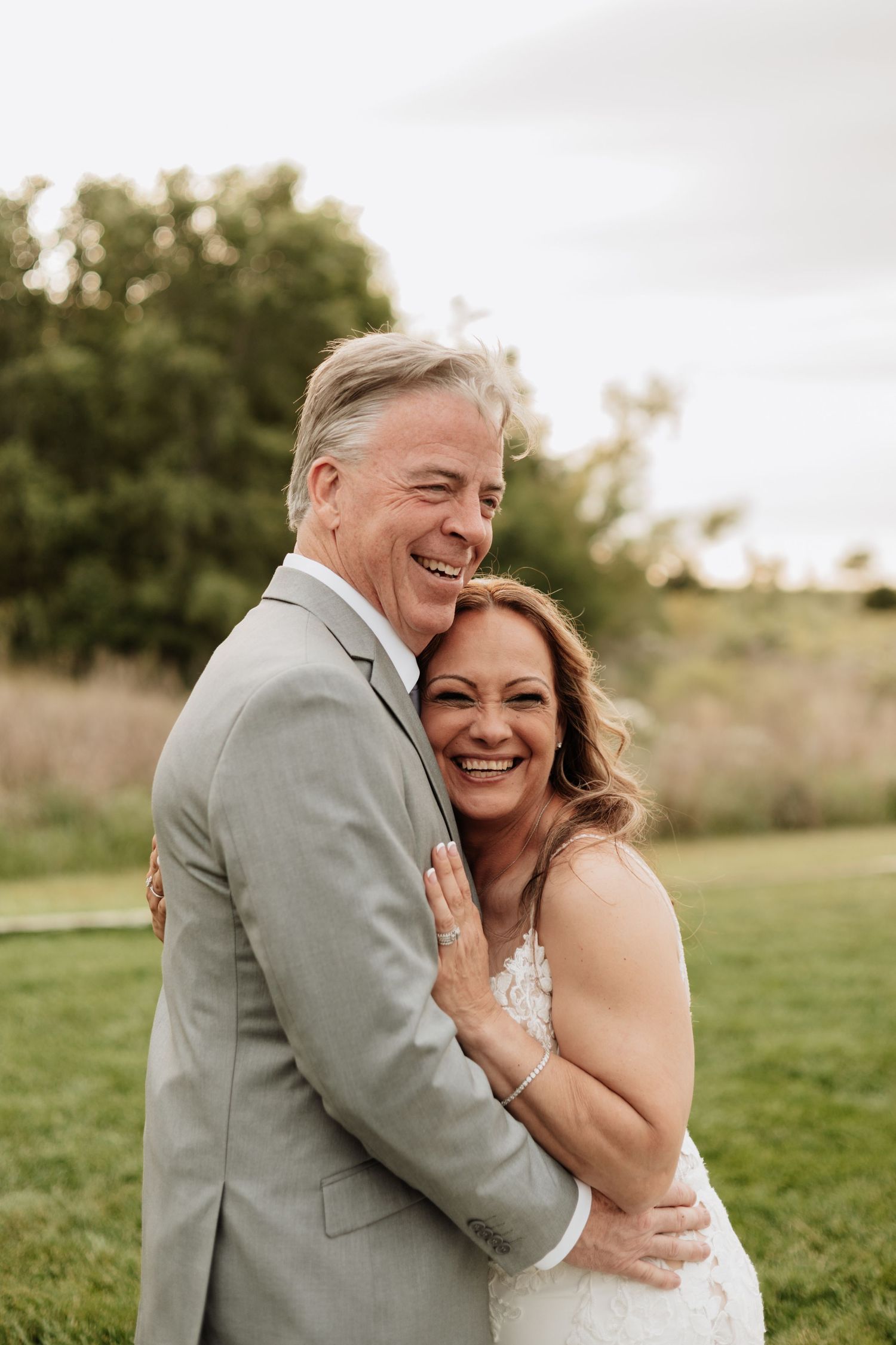 Joyful outdoor wedding portraits with couple embracing and laughing in a green field.