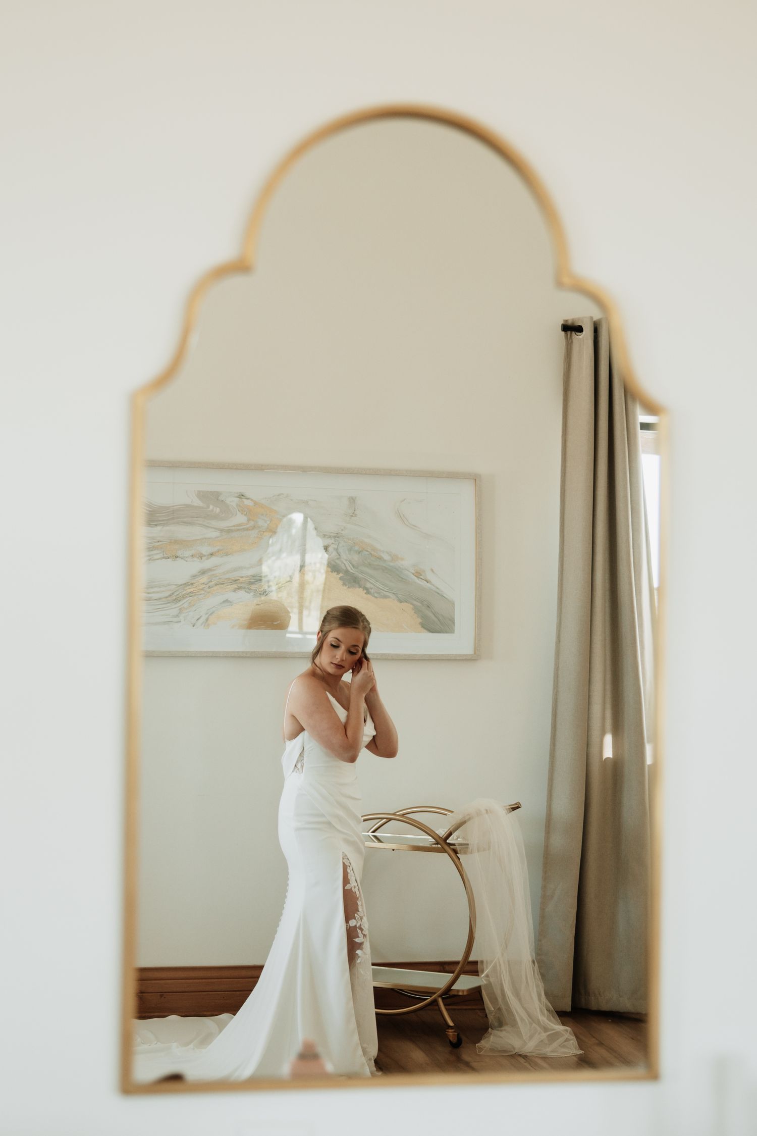 A reflection in an arched mirror shows a bride in an elegant white wedding gown.