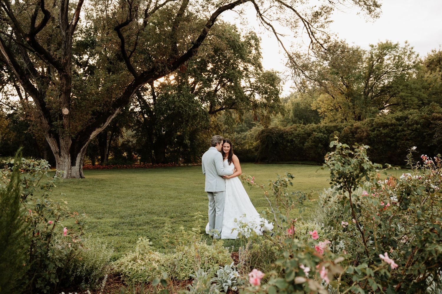 A couple shares romantic moments in a serene outdoor garden setting during their wedding photoshoot at golden hour.