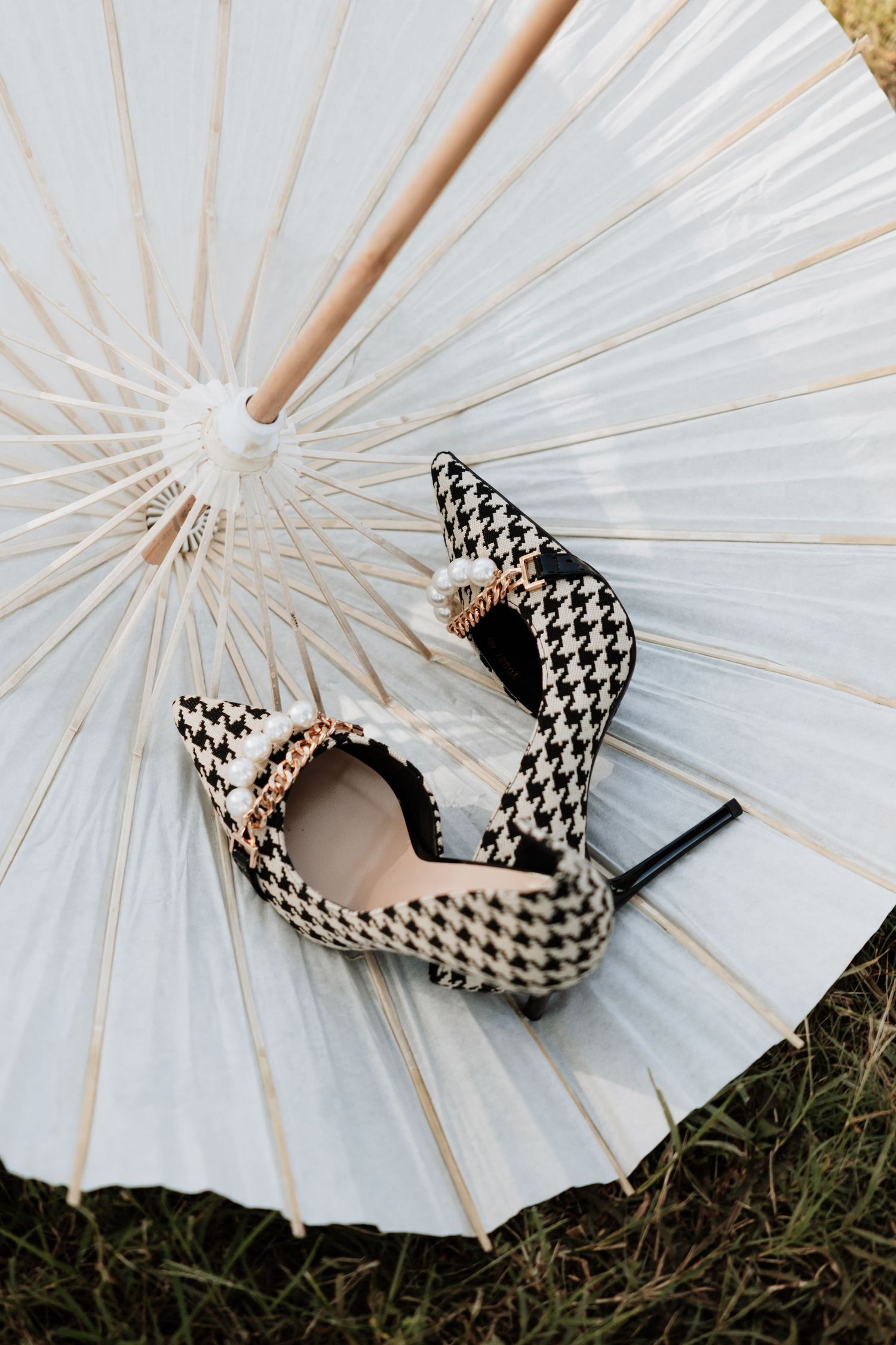 Black and white houndstooth pattern high heels placed on a white parasol against grass background.