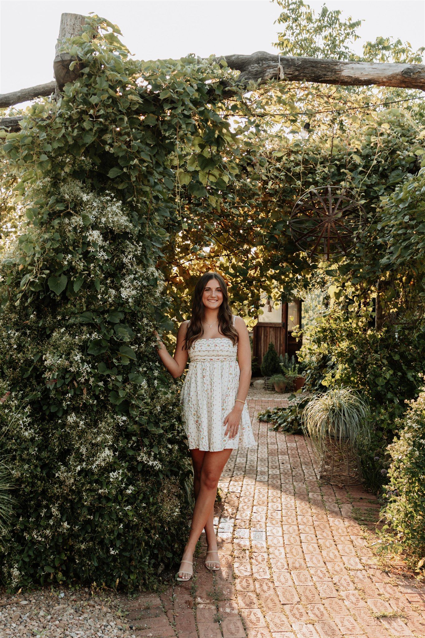 Woman in floral outfit posing along a vine-covered garden pathway.