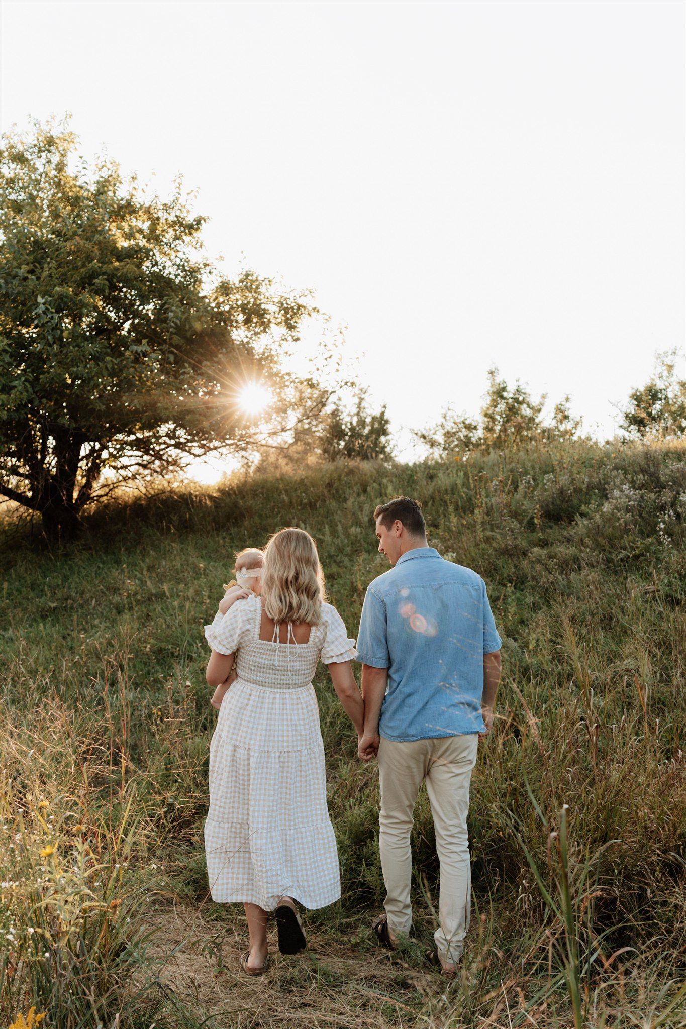 Family walking together through tall grass at sunset.