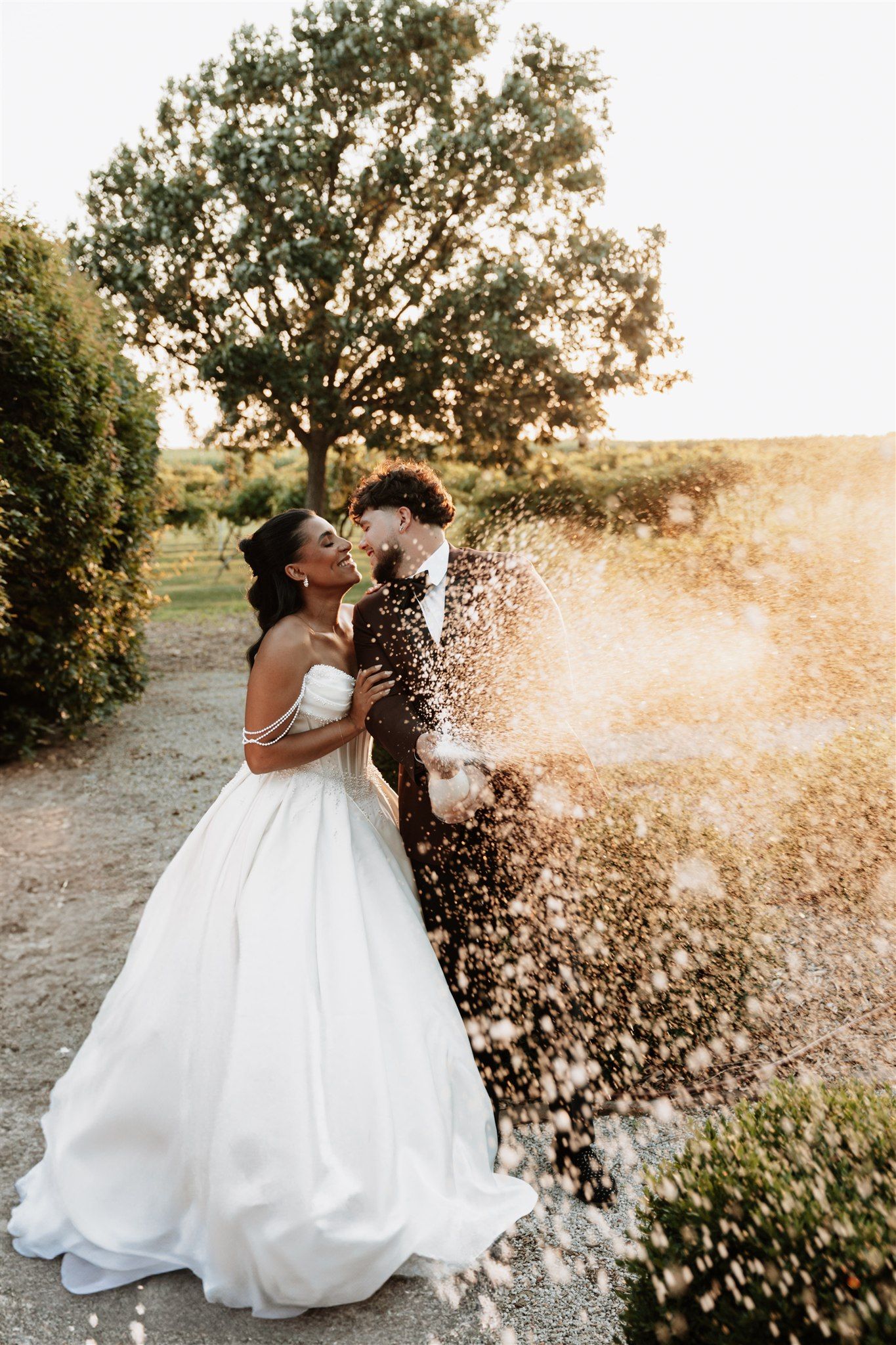 Newlyweds celebrating with champagne spray at sunset in outdoor wedding photos.
