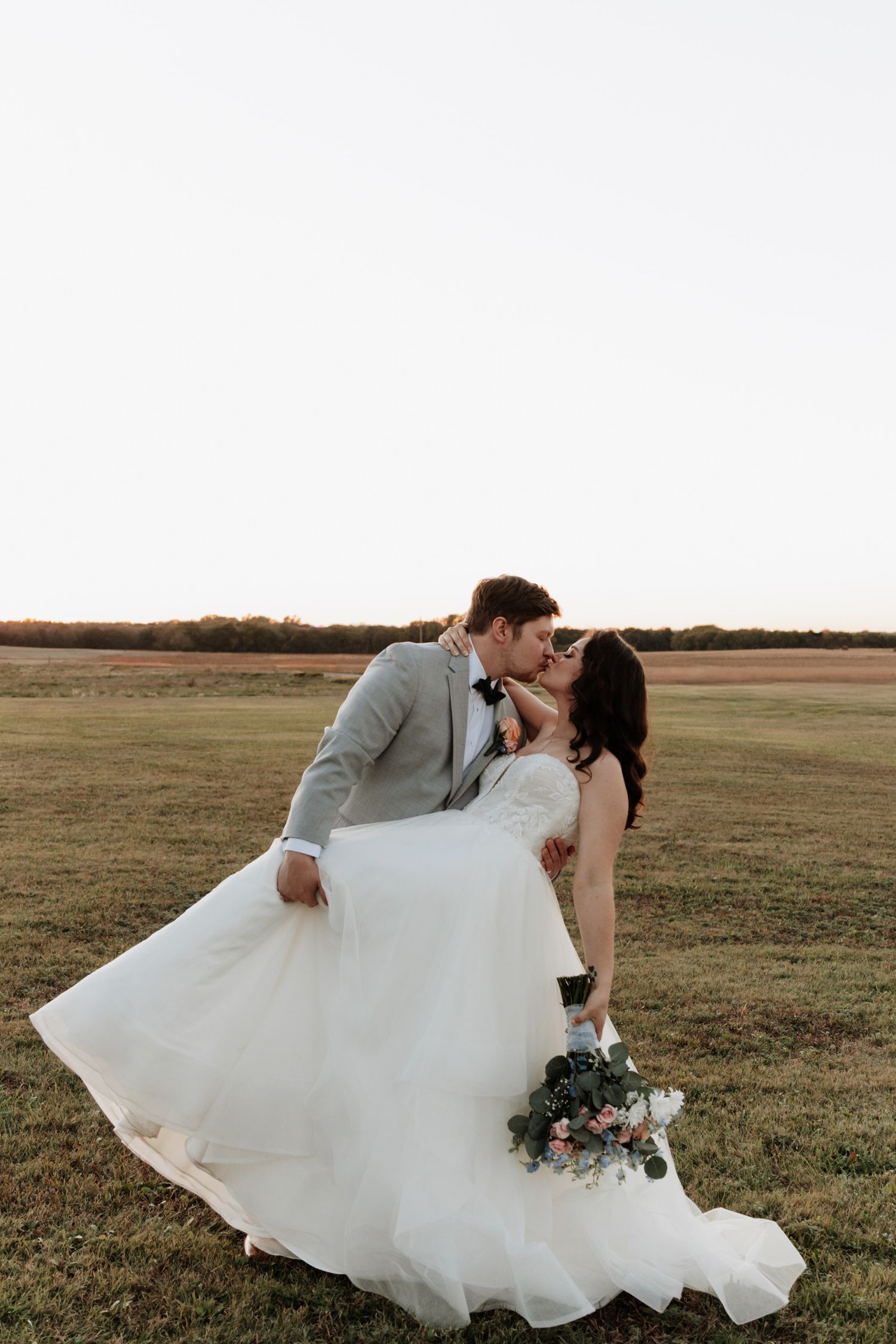 Romantic wedding couple poses in open field during sunset.