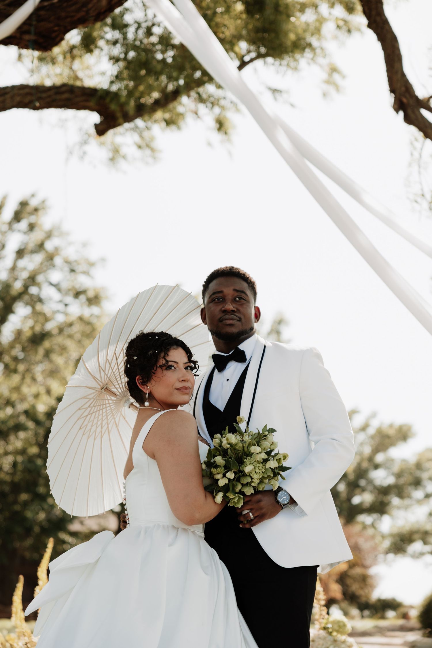 Elegant wedding portraits under white parasols with the couple in formal black and white attire.