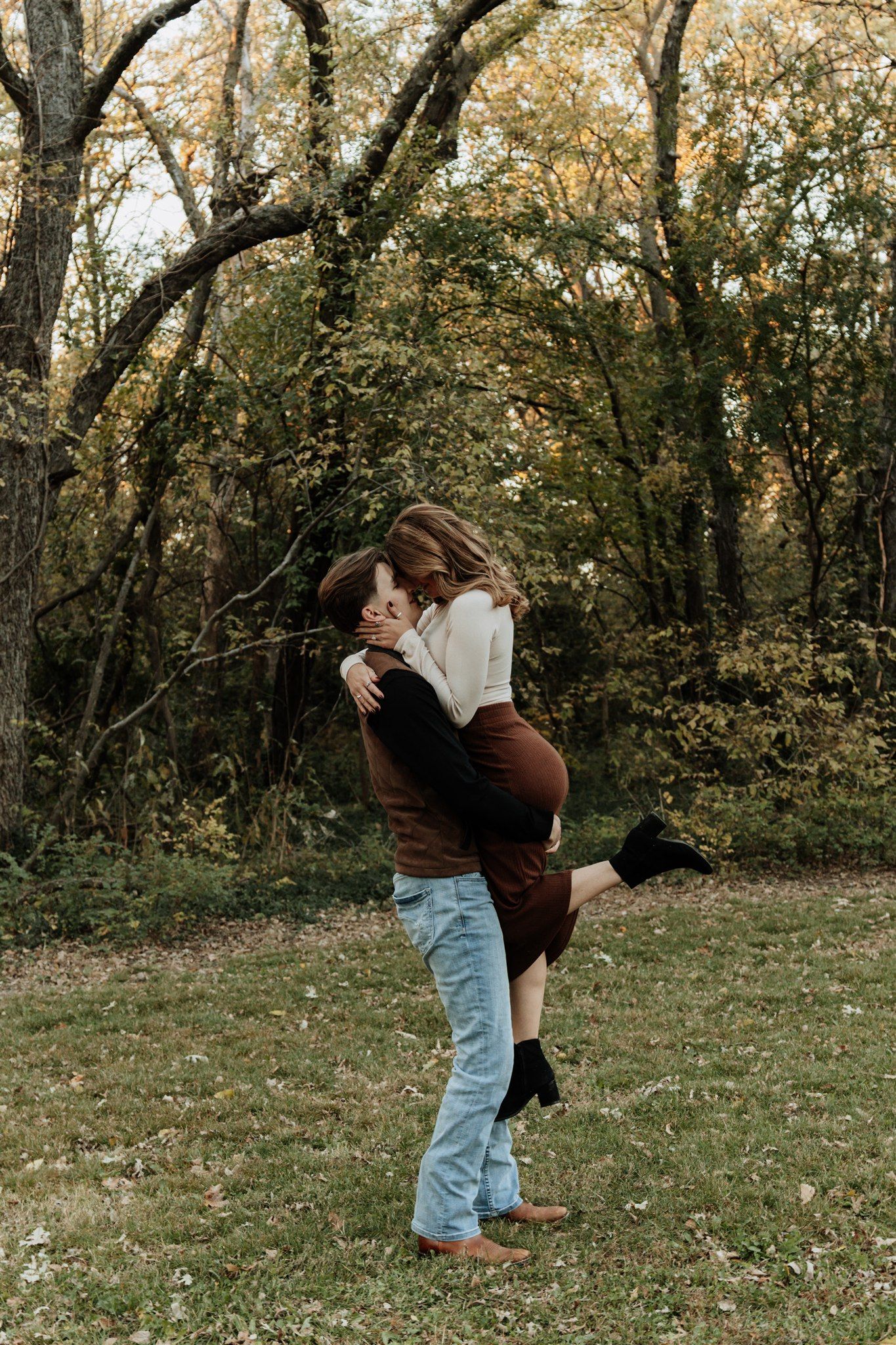 A playful couple embraces in a wooded area during autumn.