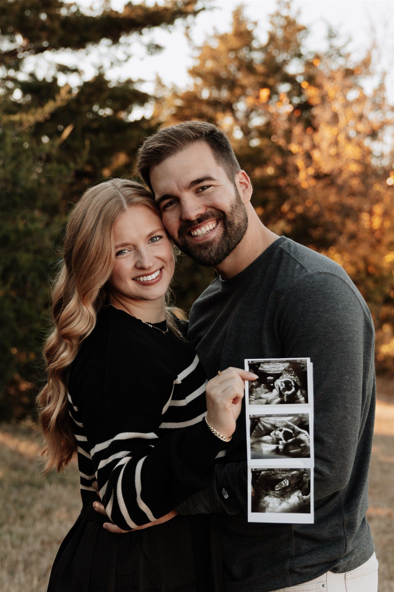 Couple in black and gray clothing holding polaroid photos during golden hour outdoors.