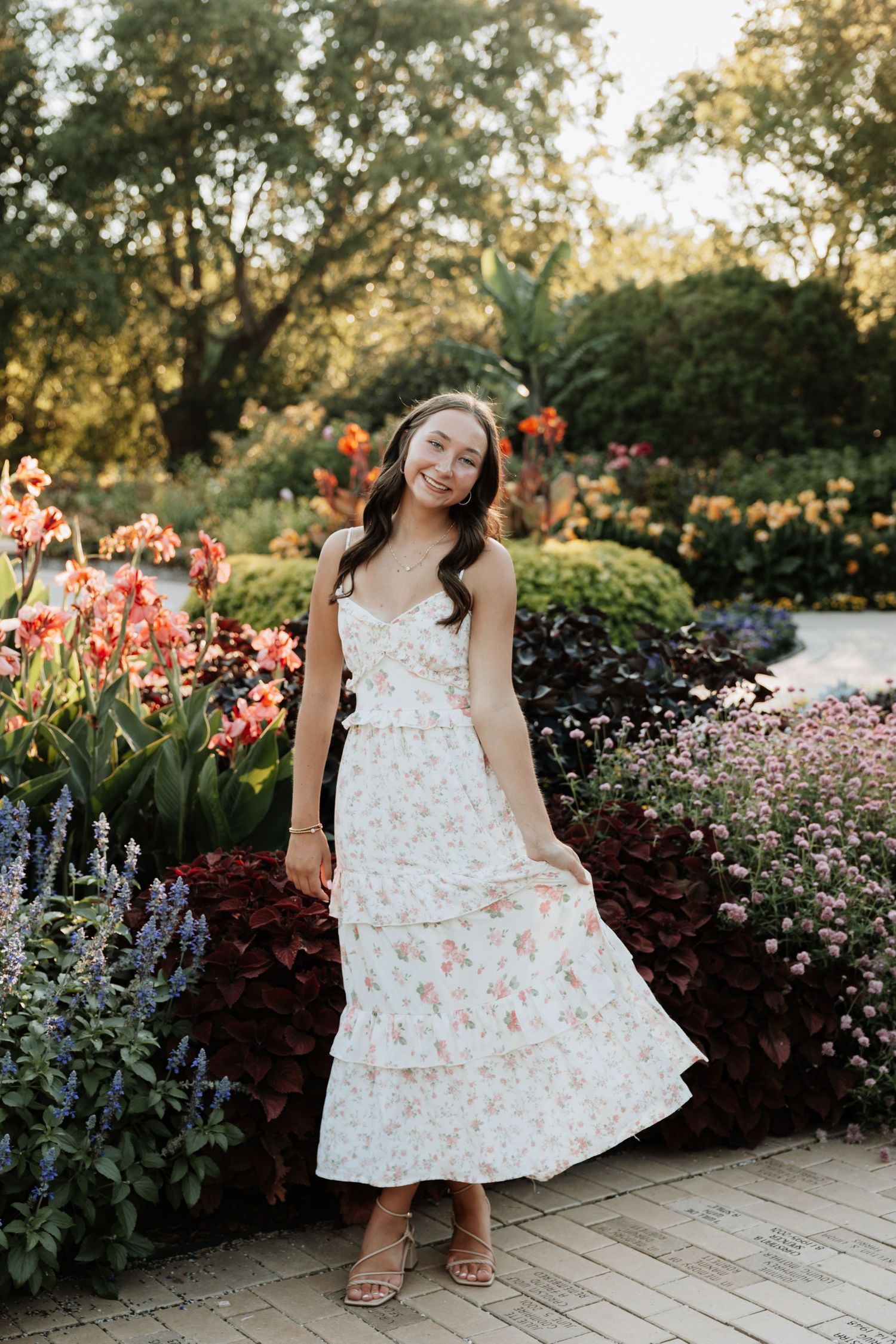 Young girl in floral dress posing in garden with blooming flowers during summer photo session.