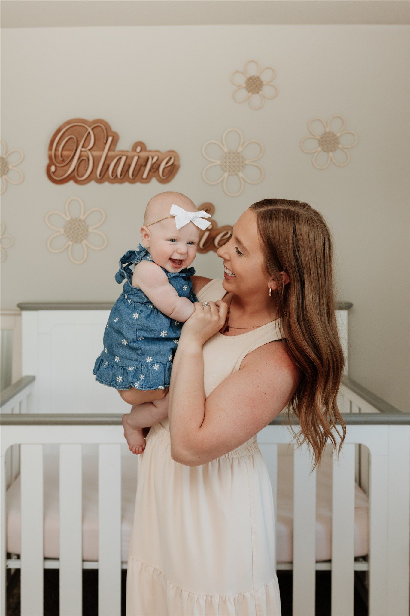 Mother and baby sharing tender moments by white crib with floral wall decor.