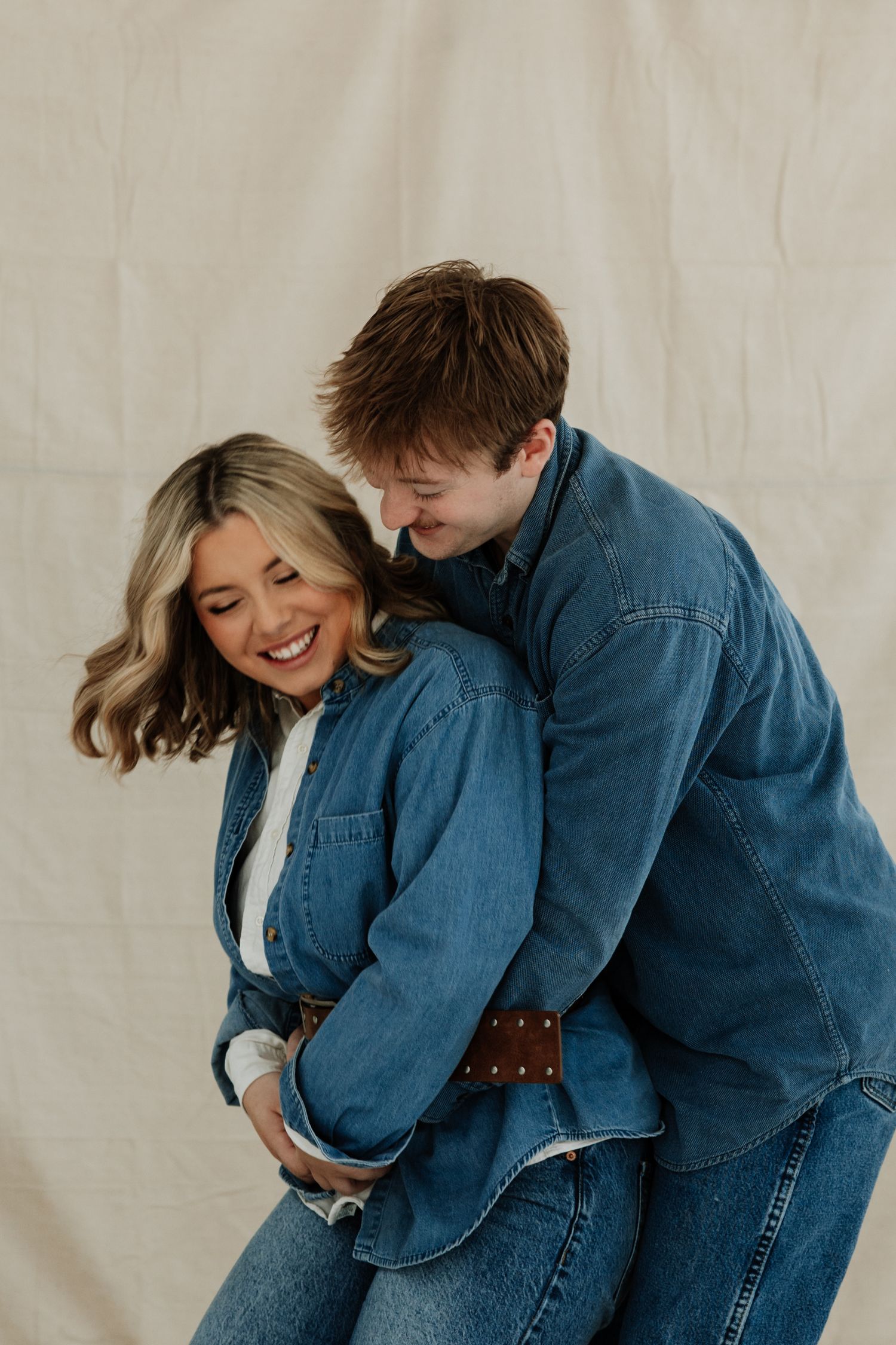 A playful couple in matching denim shares a candid moment against a neutral backdrop.