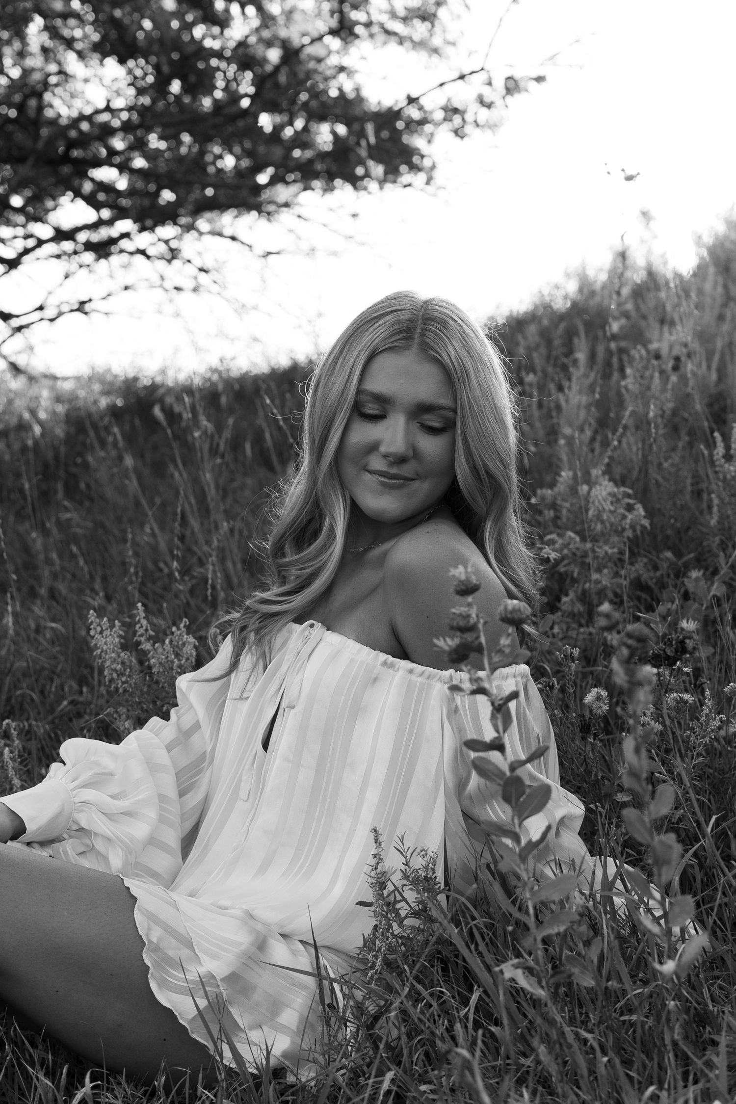 Black and white portrait of person in white ruffled dress laying in wildflower field.
