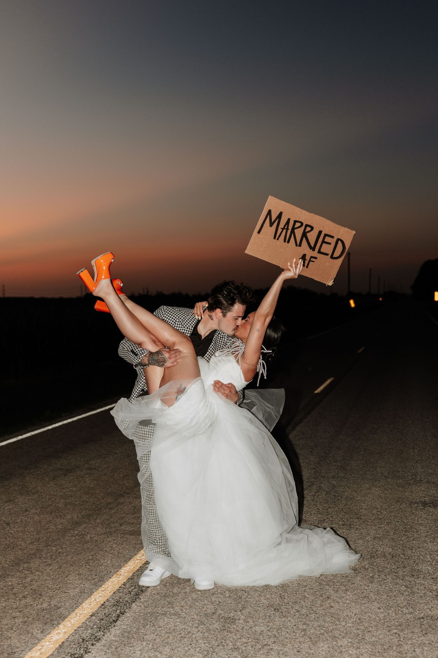 Creative nighttime wedding photo with couple laying on road holding illuminated signs.
