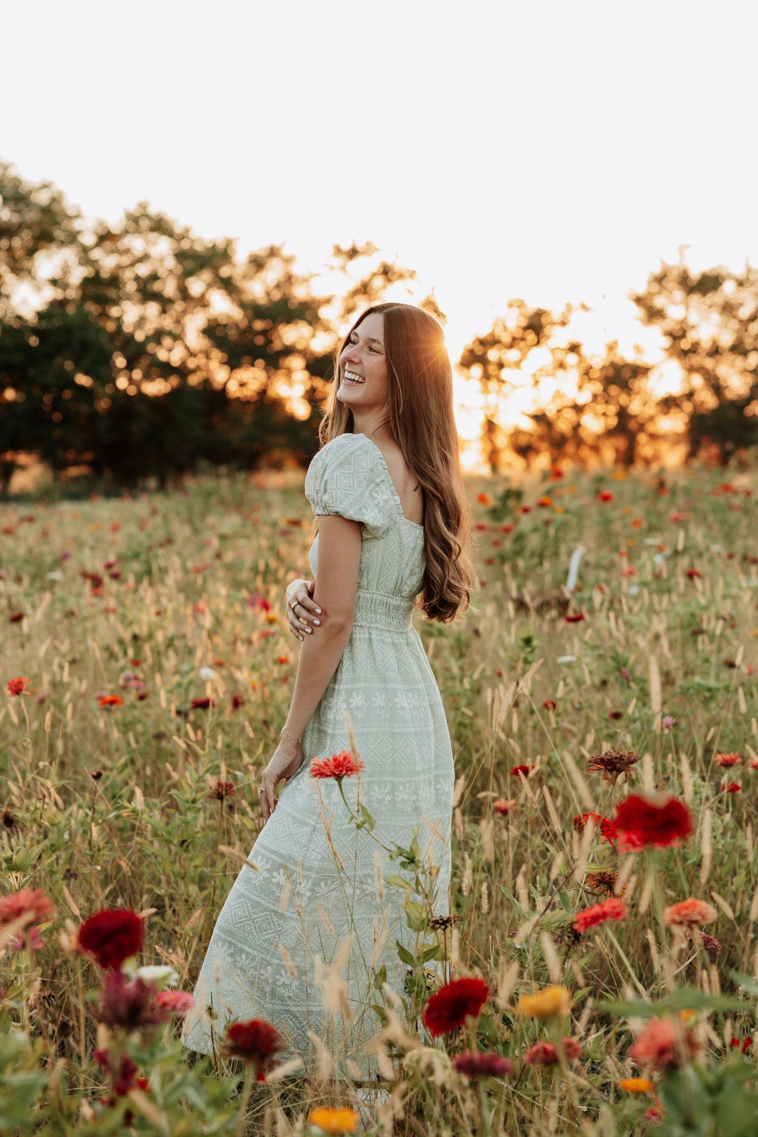 Woman in flowing white dress dancing through wildflowers during sunset.