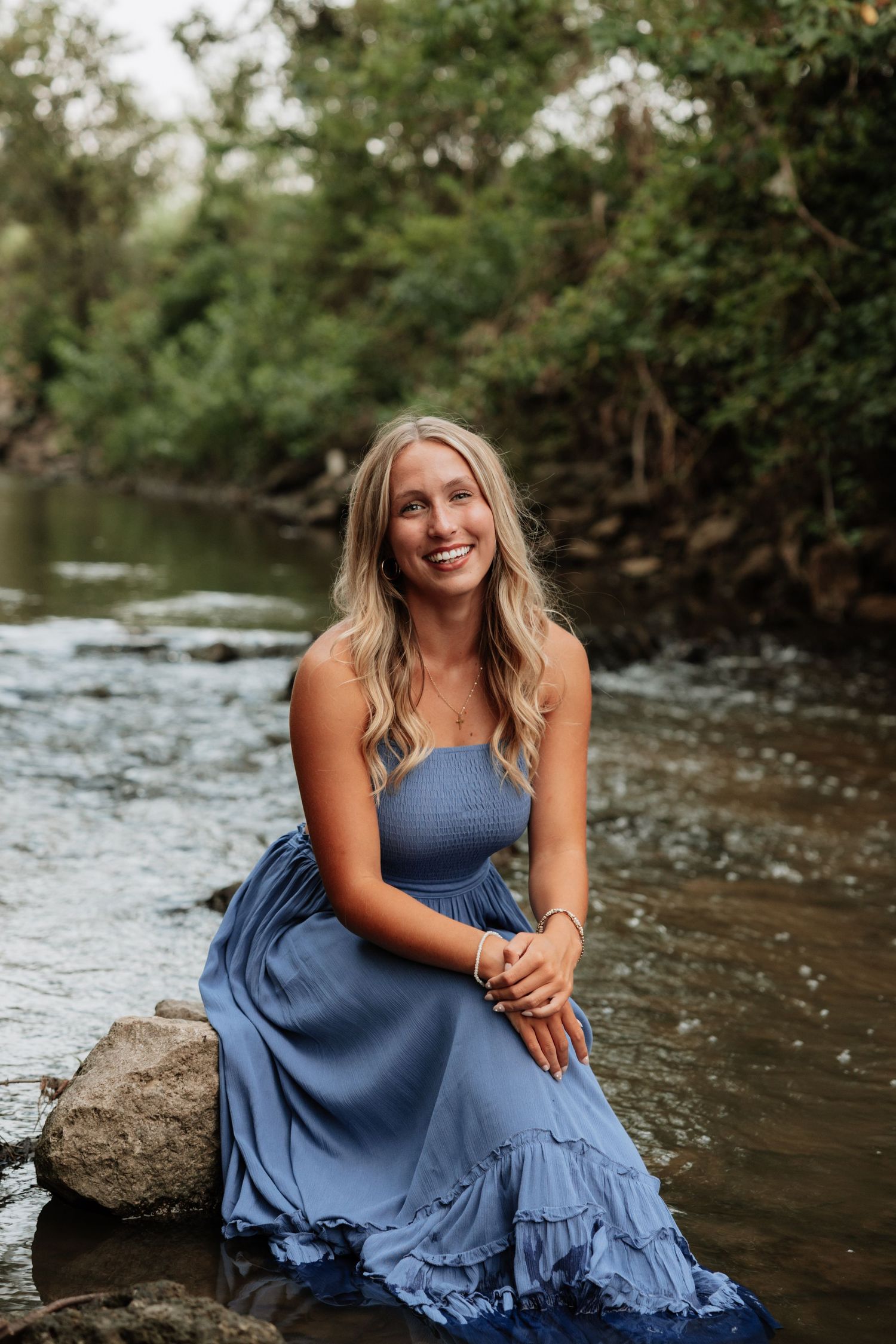 Subject in blue ruffled dress sits gracefully by a flowing stream.