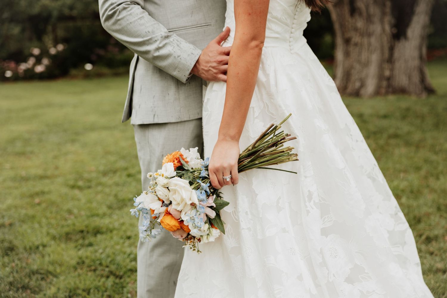 Close-up details of wedding attire and floral bouquet in outdoor garden setting.