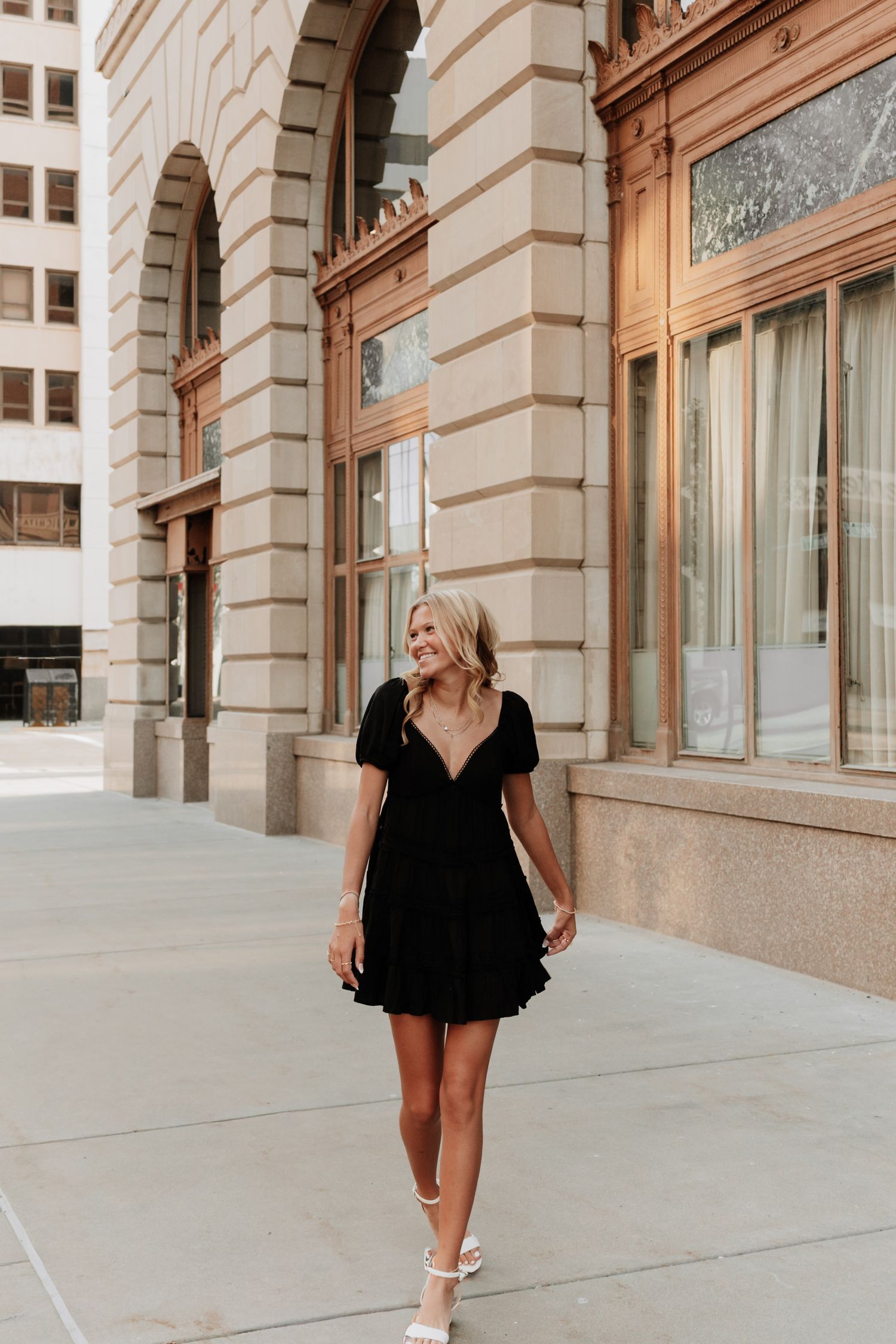 Fashion portraits of woman in black dress walking along urban building with classic architecture.
