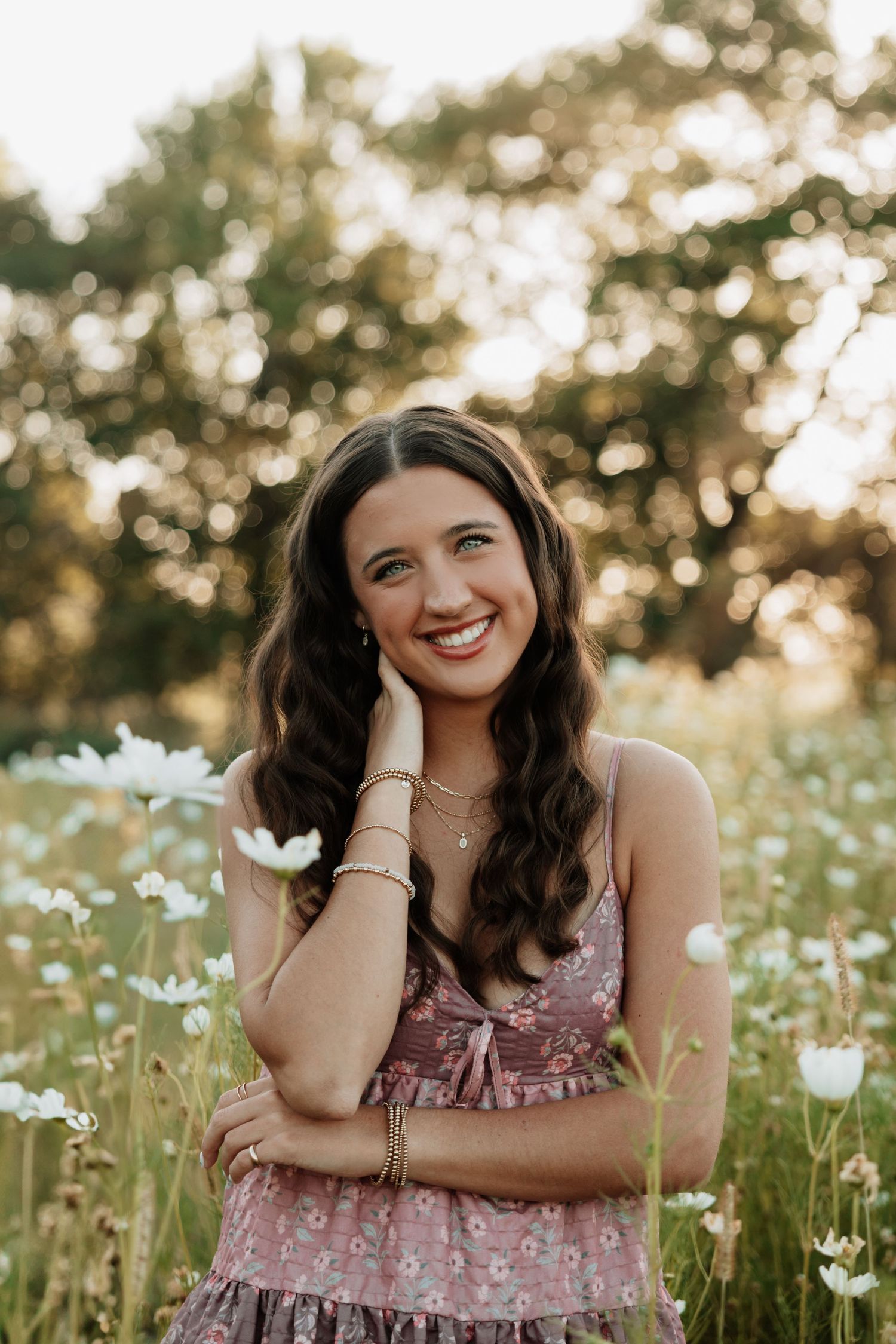 Person in pink floral dress posing playfully in a wildflower meadow at sunset.