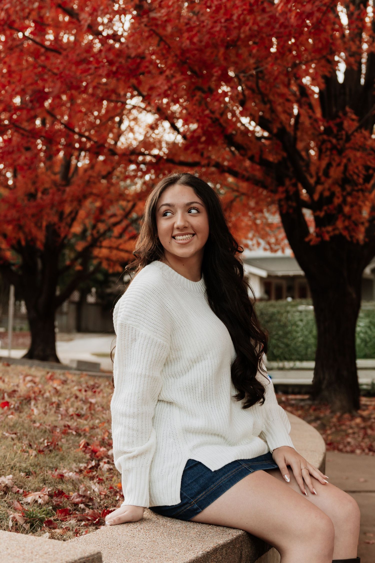 Autumn portrait session with person in white sweater against vibrant red fall foliage.