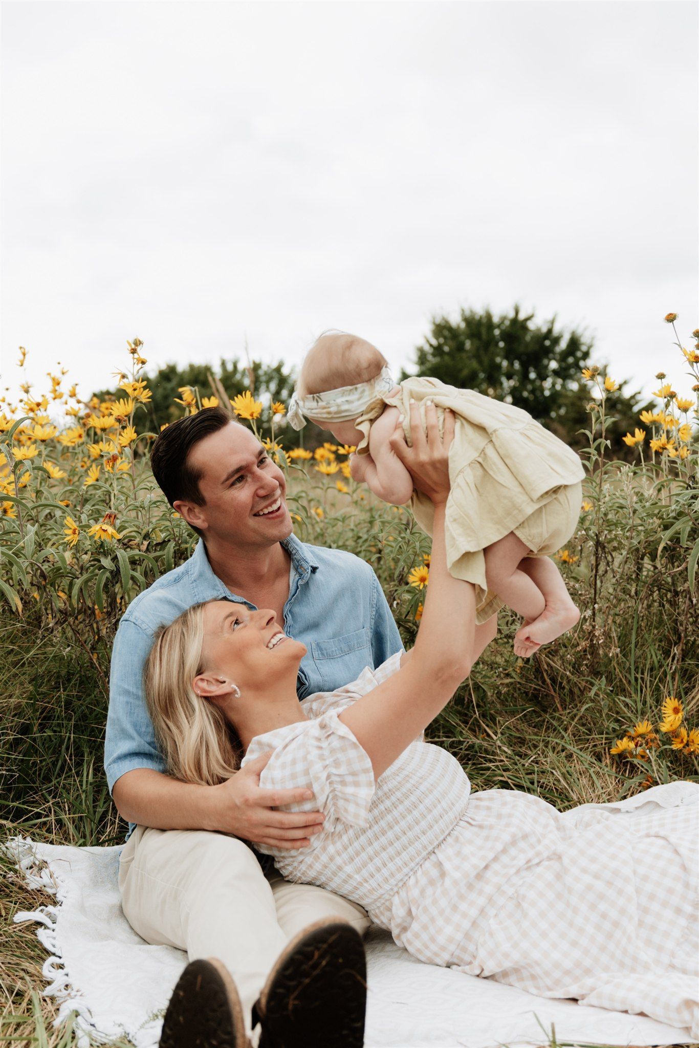 Couple laying on blanket in sunflower field sharing playful moments during sunset photoshoot.
