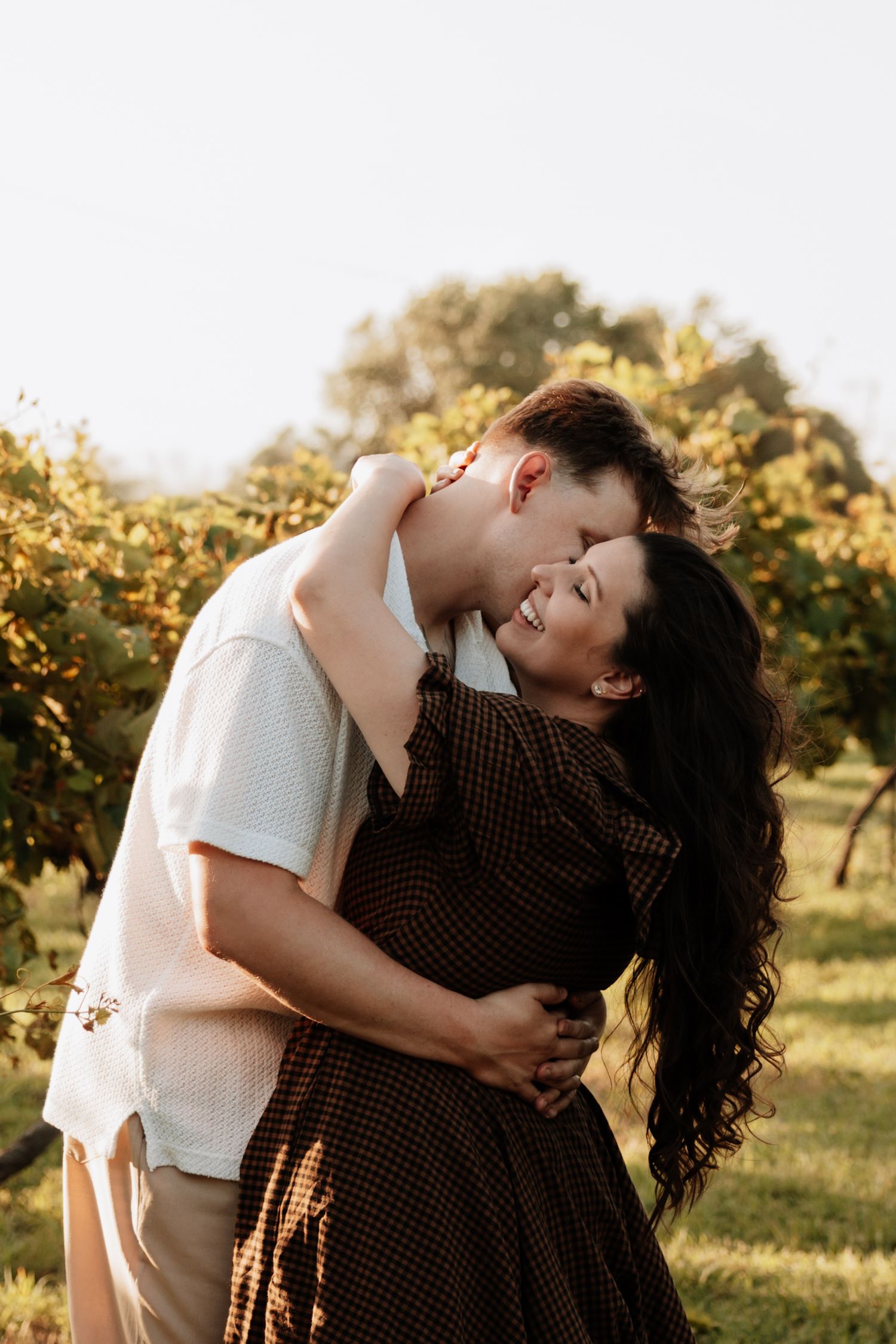 A couple shares an intimate embrace in a sun-drenched vineyard during sunset.