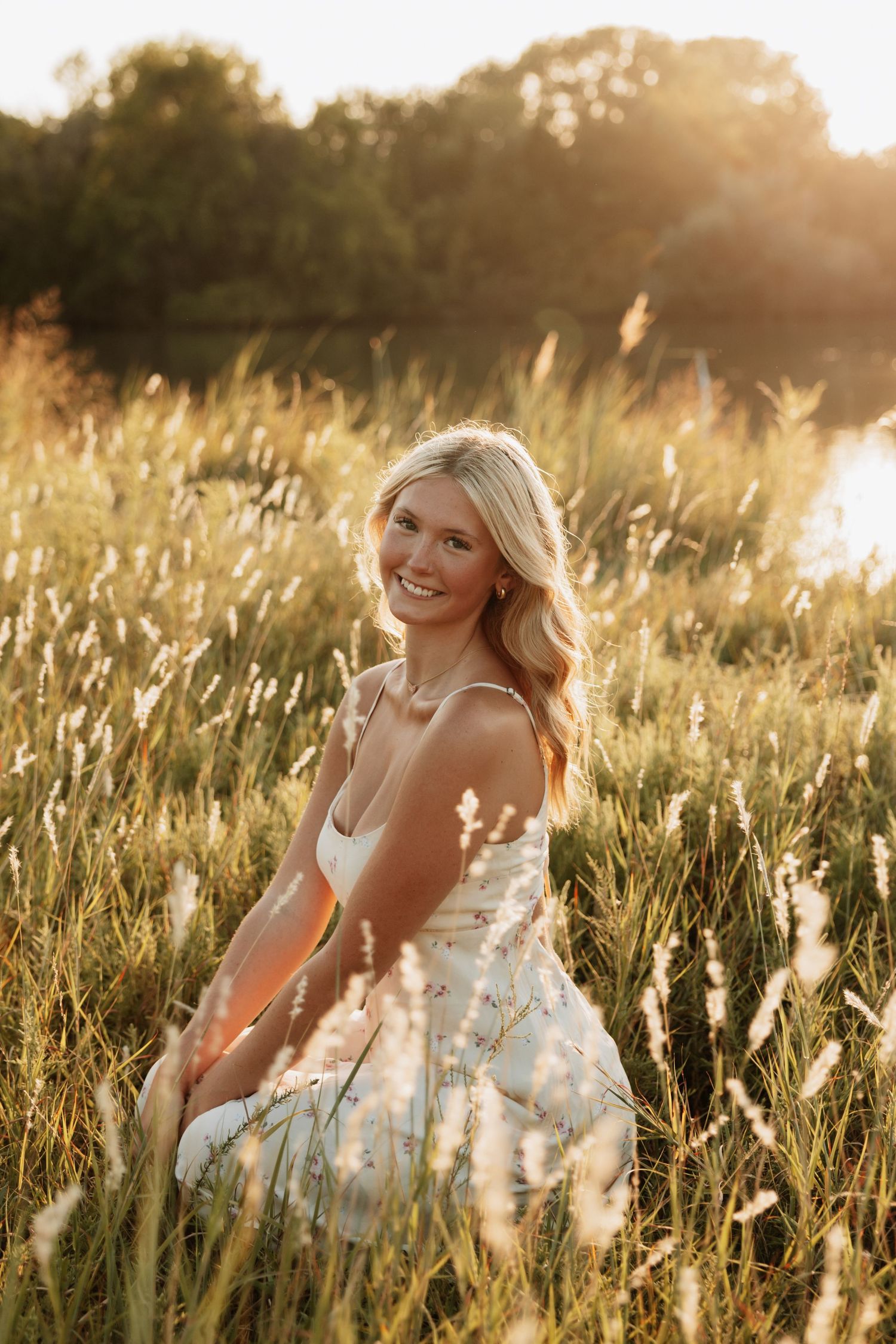 Woman in white dress posing gracefully in tall grass during golden hour.