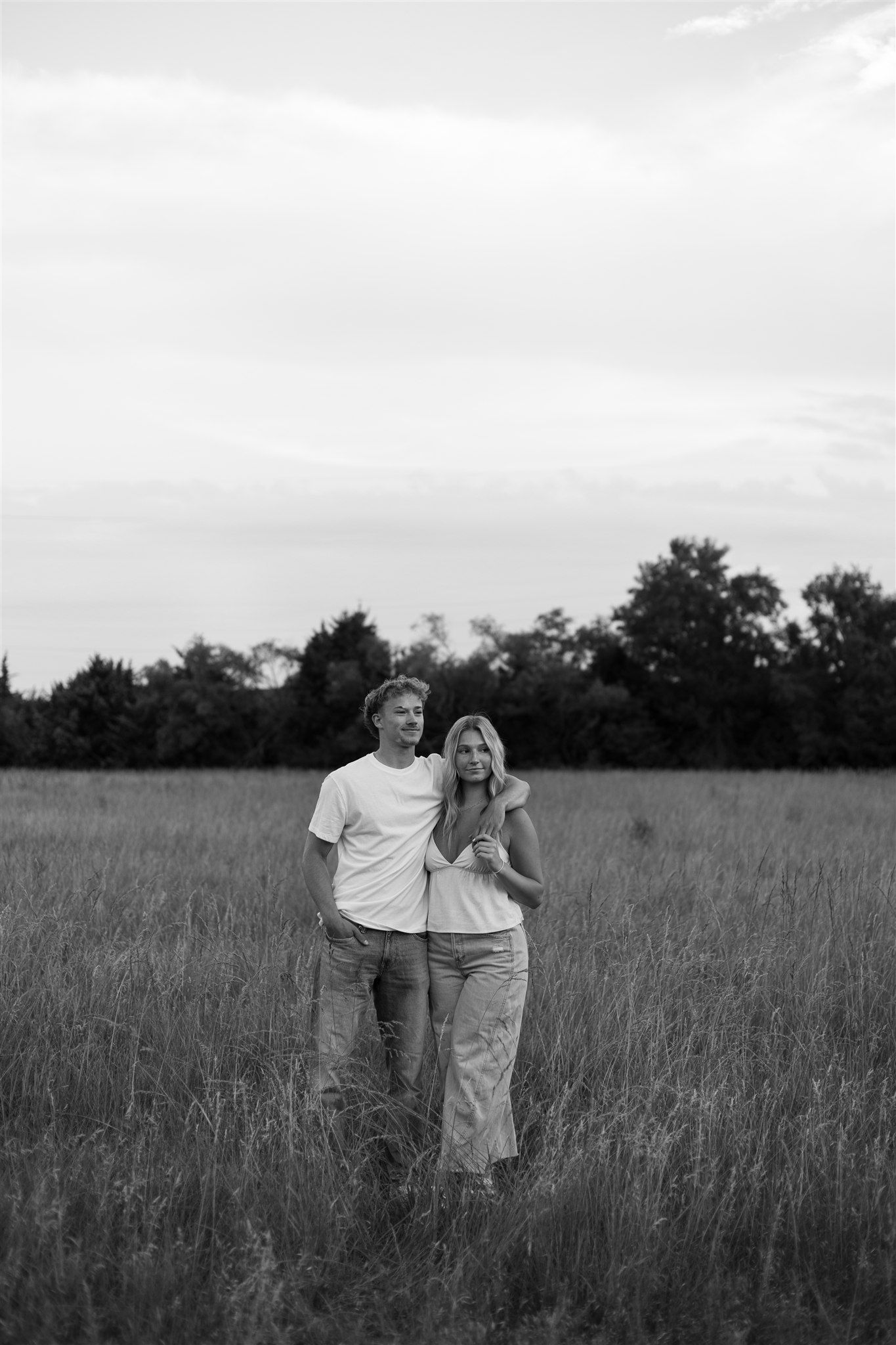 A couple stands together in a serene meadow of tall grass during twilight.