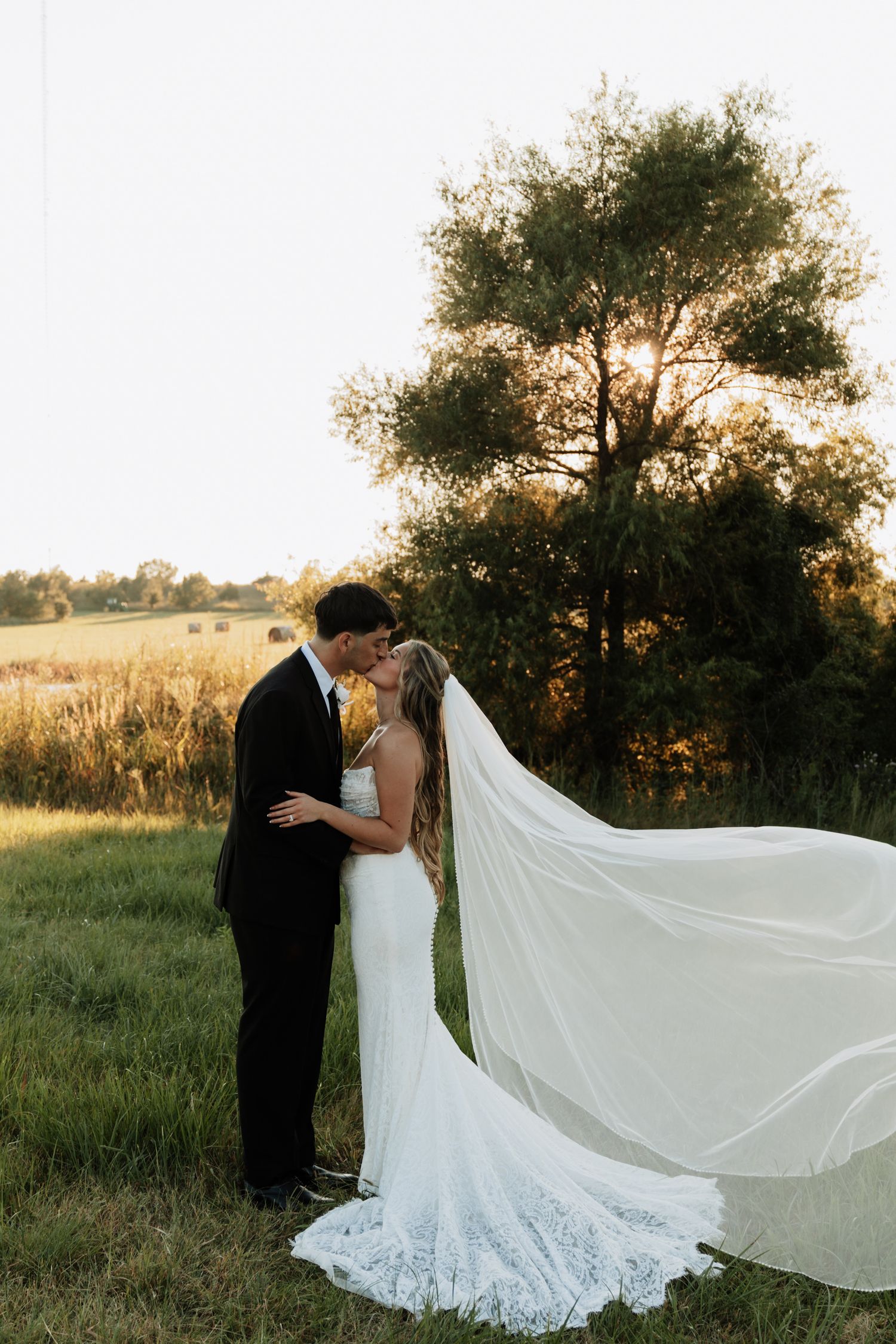 Romantic sunset wedding portraits in field with flowing veil and lace dress.