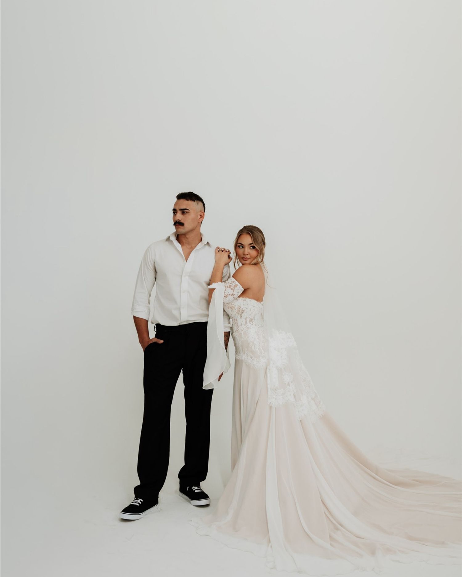 Minimalist wedding portraits against white backdrop showing flowing white dress and formal attire.