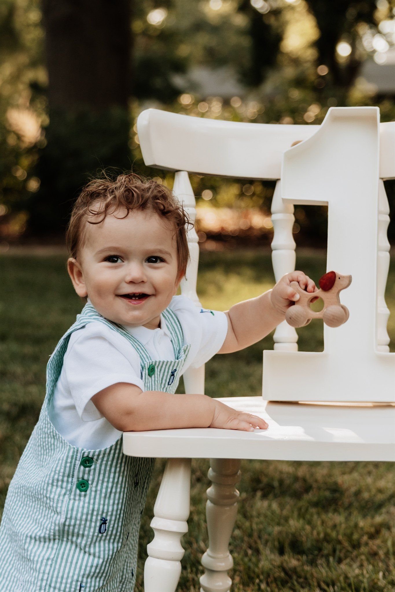 Baby in striped outfit playing with white furniture outdoors.