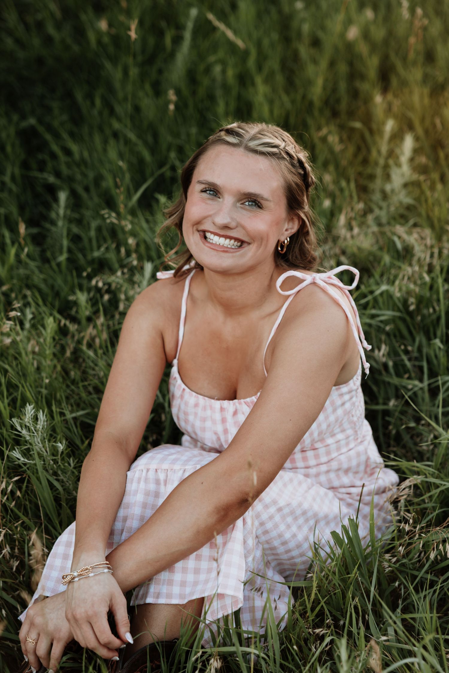 Candid summer portrait of someone in a white gingham dress laying in tall grass.