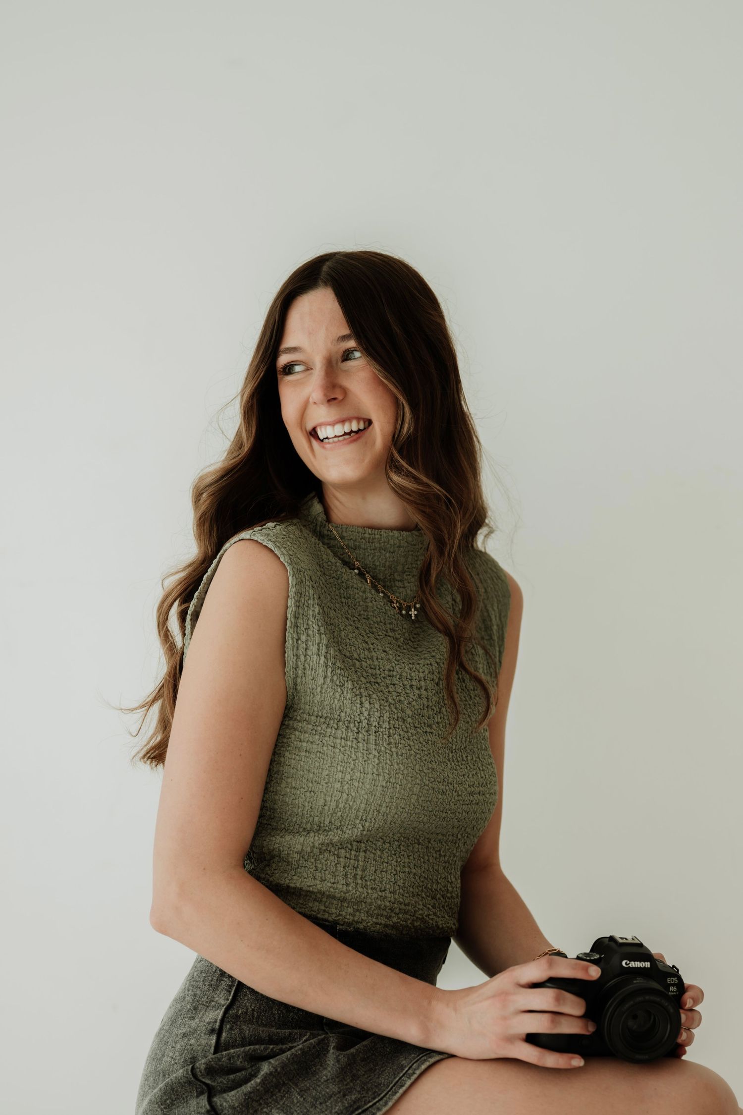 Portrait session showing a photographer in an olive green top holding a camera against white background.