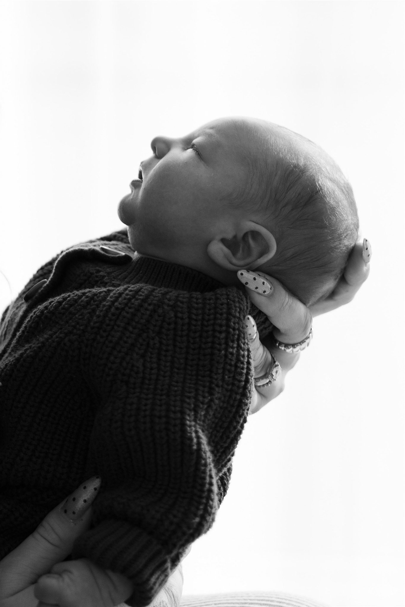 A silhouette of an infant being lifted against a bright white background.